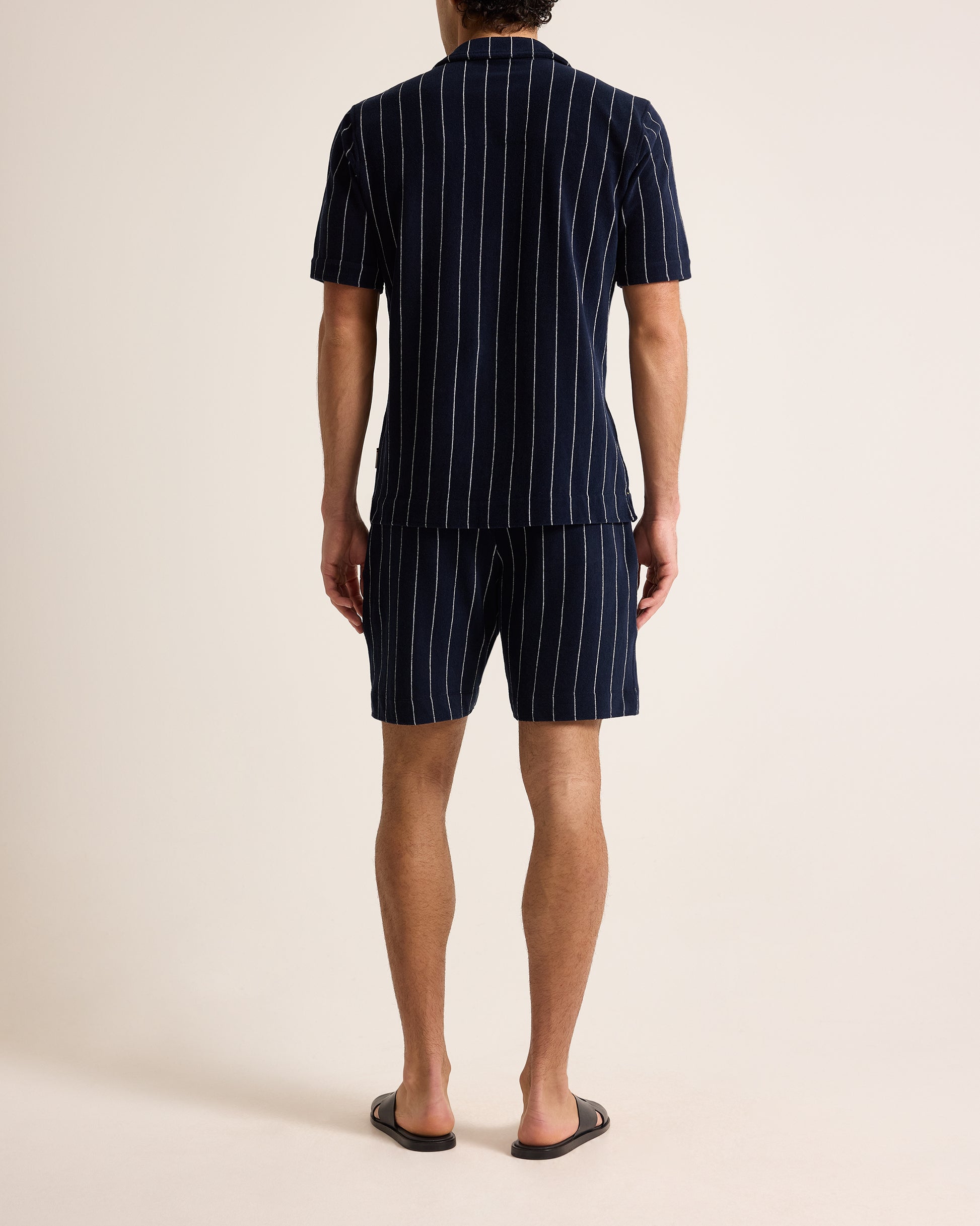 Person wearing a navy pinstripe shirt and shorts set on a beige background