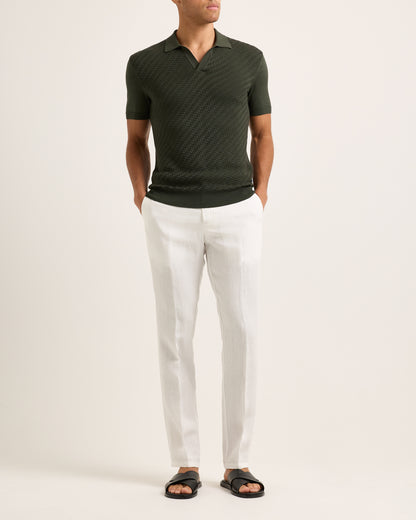 Model wearing a green polo shirt and white pants on a plain background