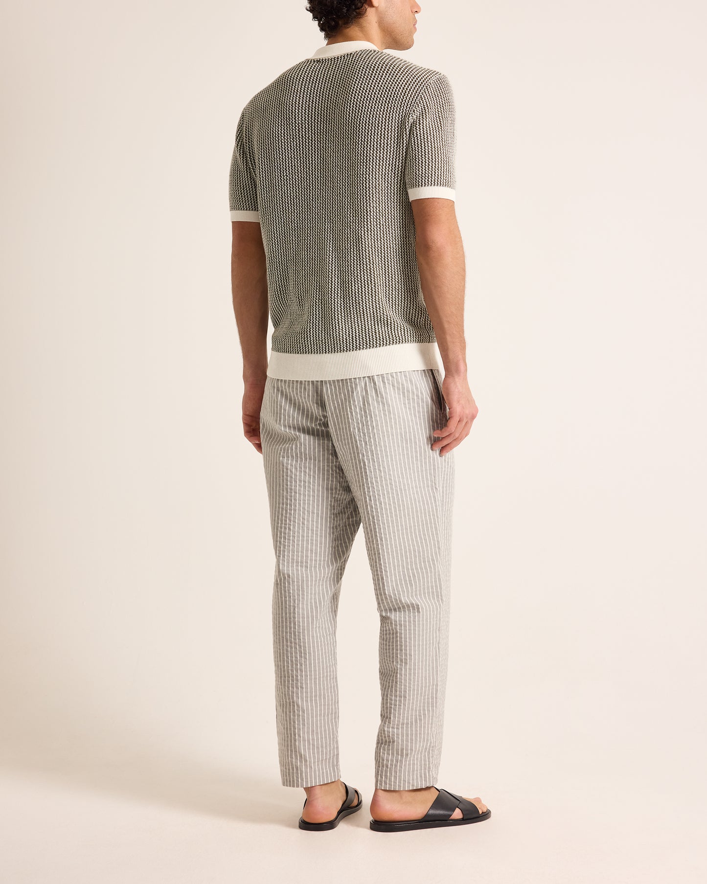 Person wearing a gray ribbed t-shirt and striped pants on a plain background