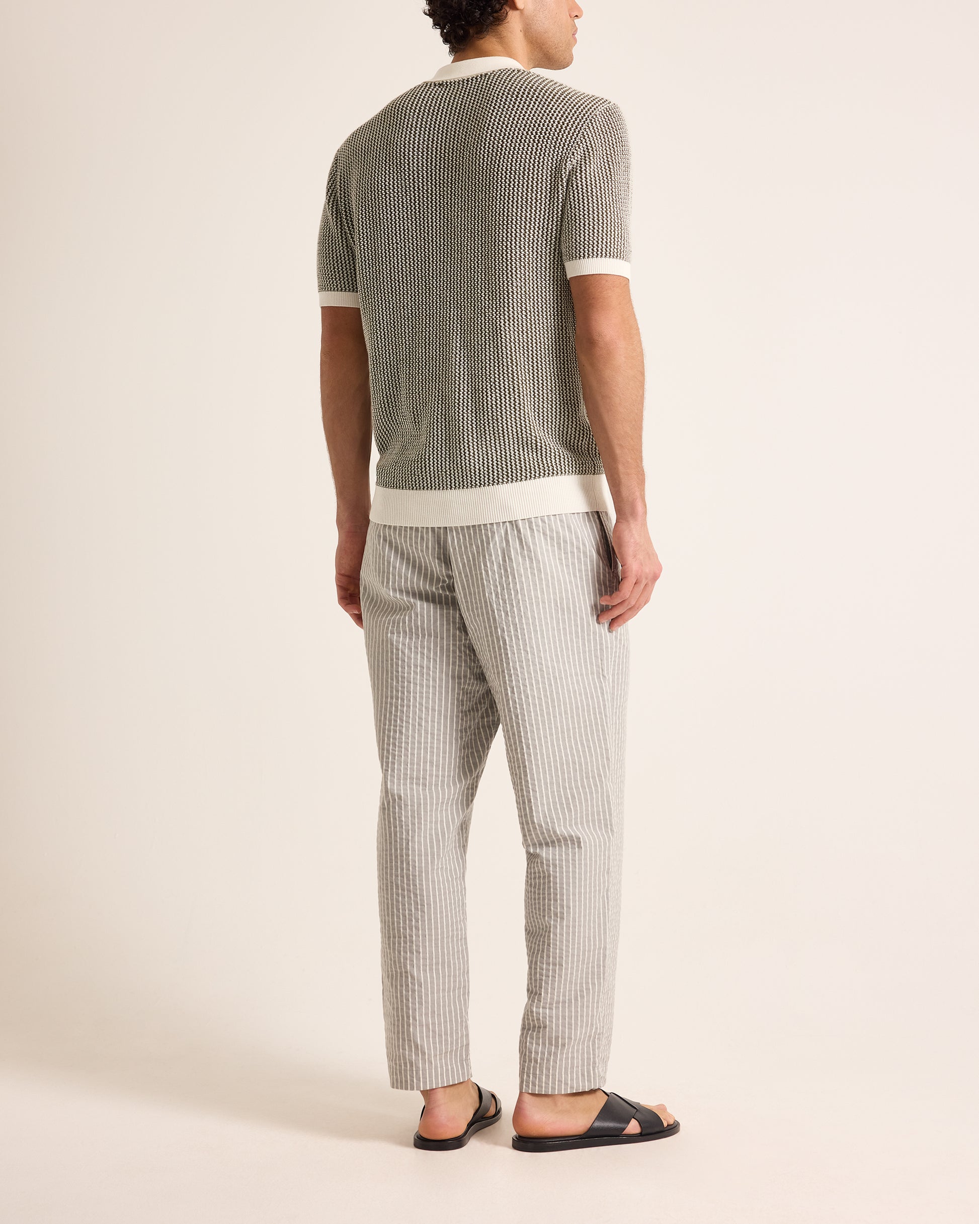 Person wearing a gray ribbed t-shirt and striped pants on a plain background