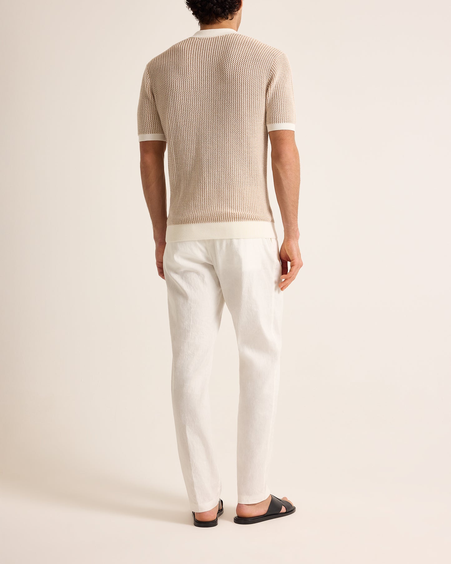 Person wearing a beige ribbed sweater and white pants on a plain background