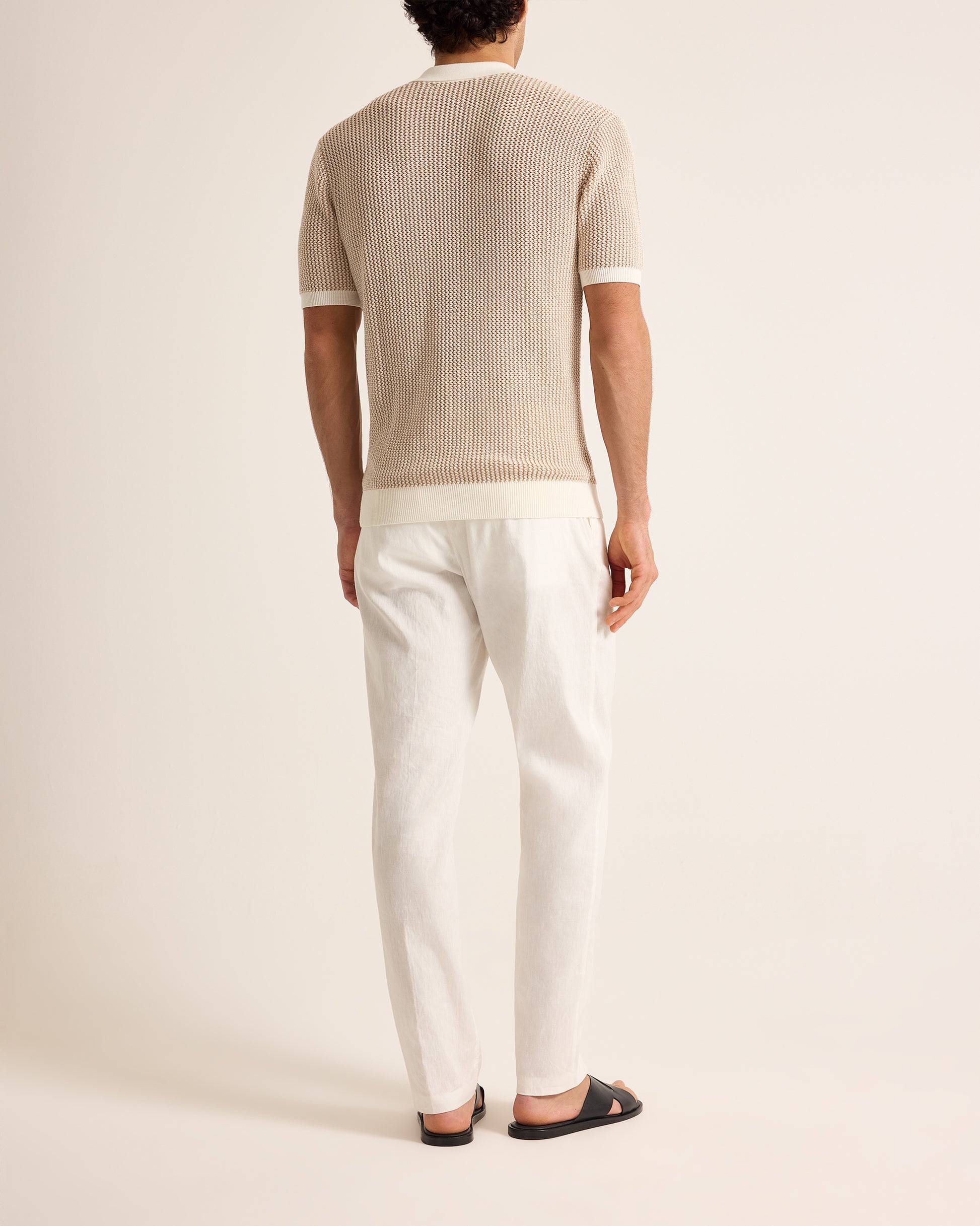 Person wearing a beige ribbed sweater and white pants on a plain background