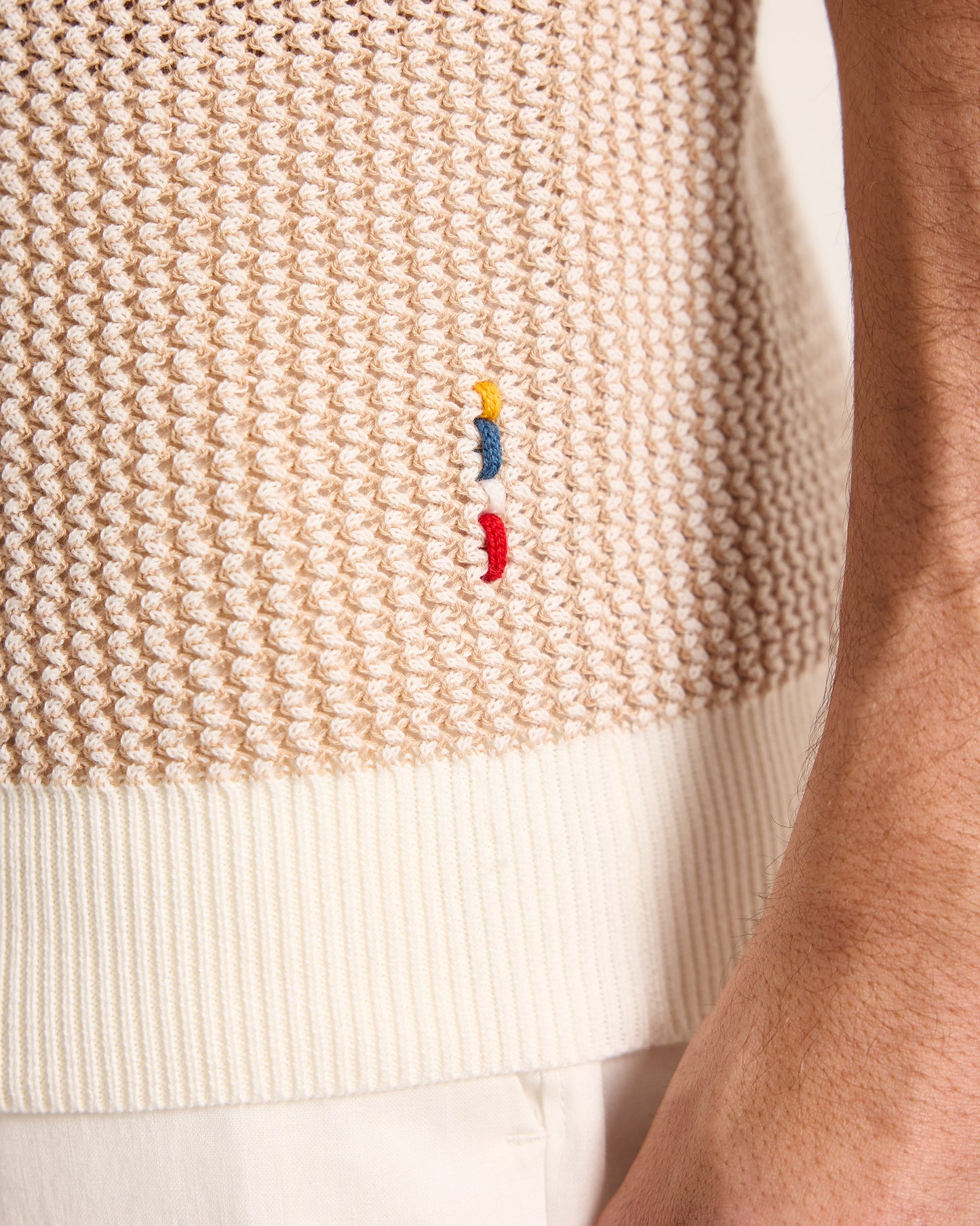 Close-up of a beige knitted sweater with embroidered colorful logo.
