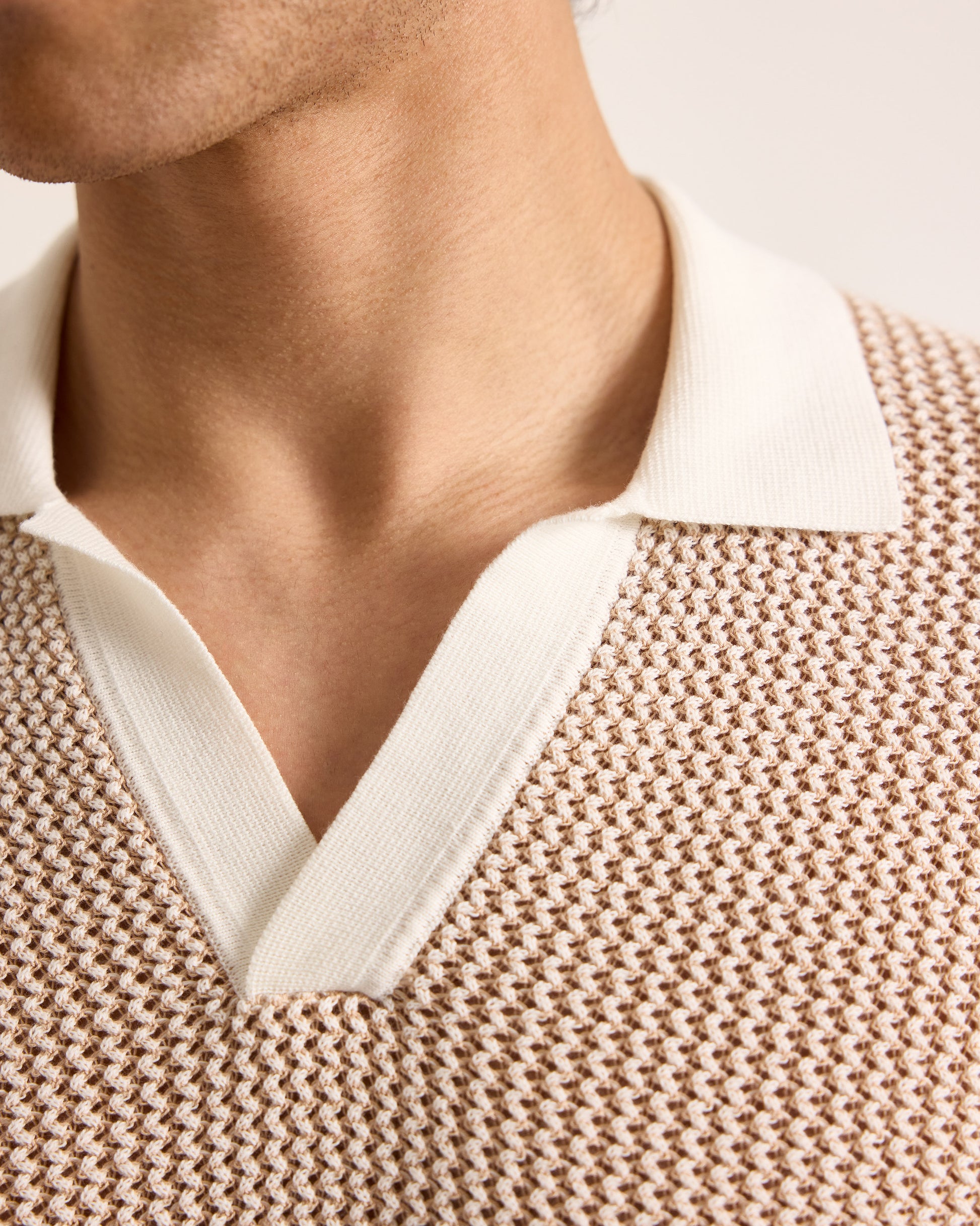 Close-up of a person wearing a beige knitted sweater with a white collar.