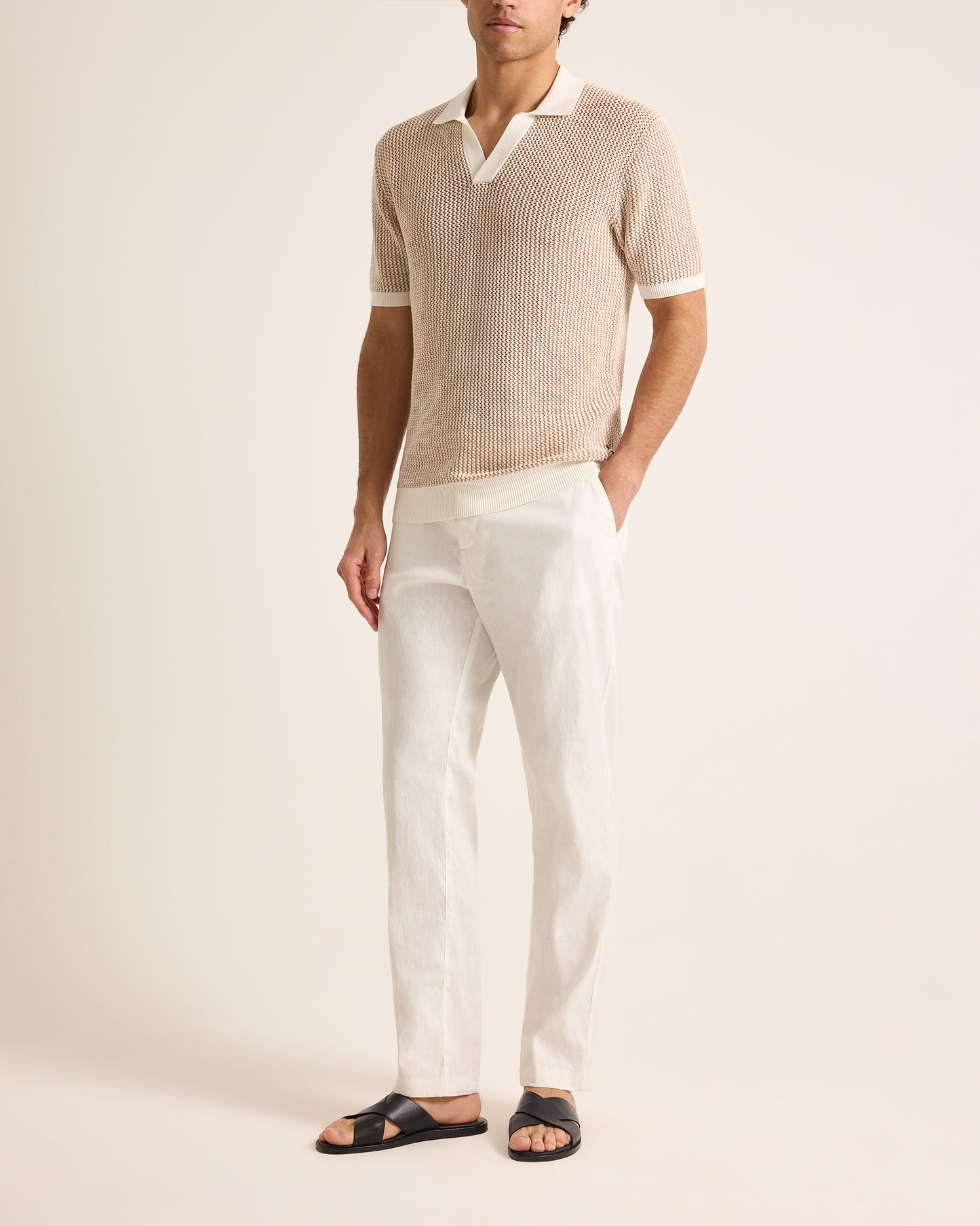 Man wearing a beige ribbed sweater and white pants on a plain background