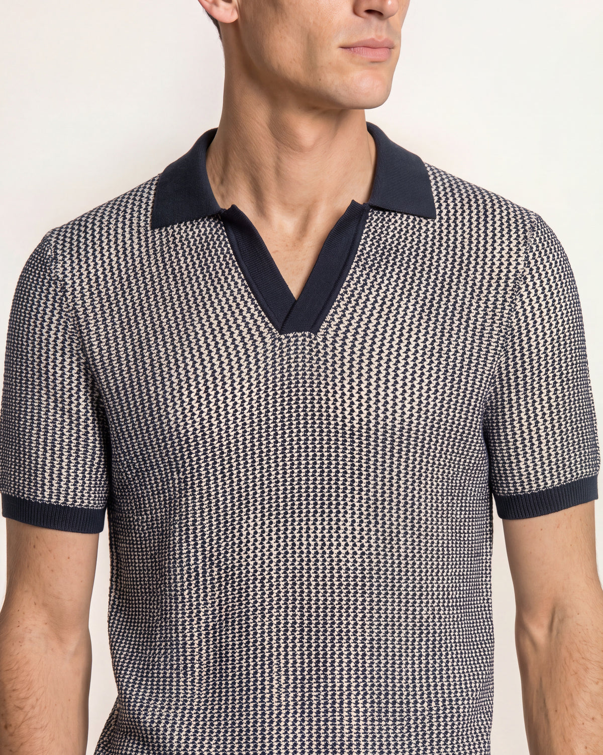 A close-up of a man wearing a short-sleeve polo shirt with a fine black and white micro-pattern, featuring solid dark navy blue trim on the collar and sleeve cuffs.