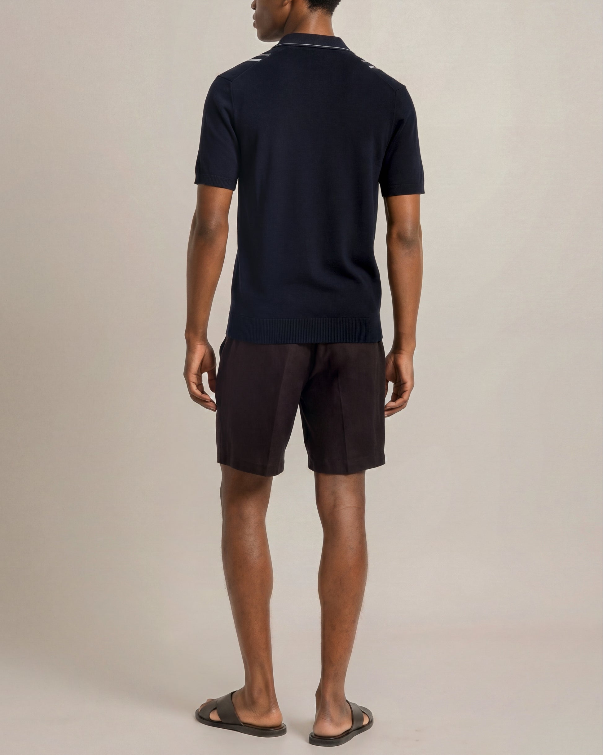 Man wearing a navy polo shirt and dark shorts on a beige background