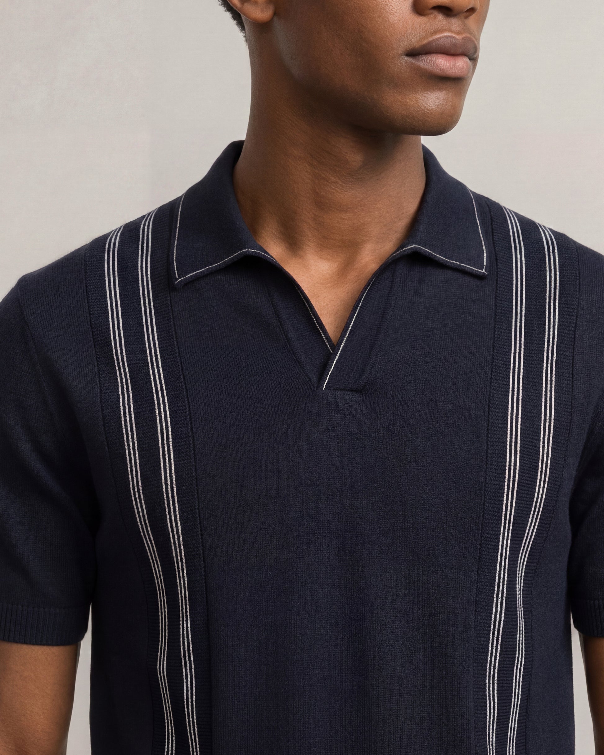 Man wearing a navy blue polo shirt with white stripes on a neutral background
