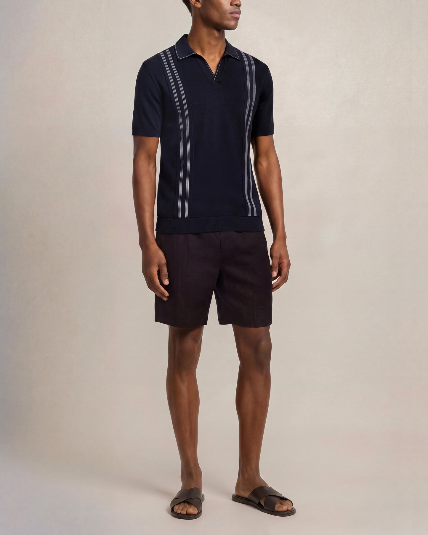 Man wearing a navy polo shirt with white stripes and black shorts on a beige background