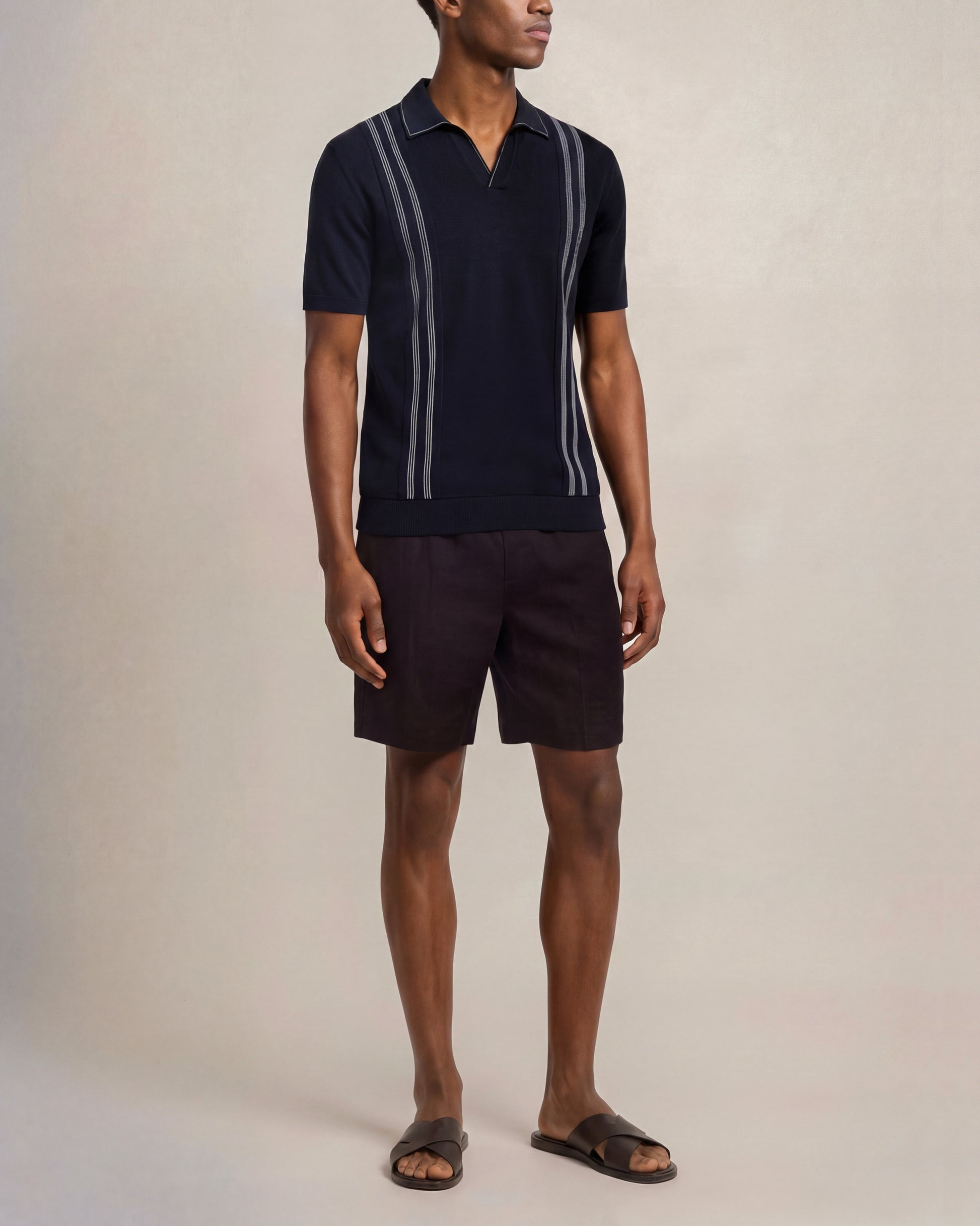 Man wearing a navy polo shirt with white stripes and black shorts on a beige background
