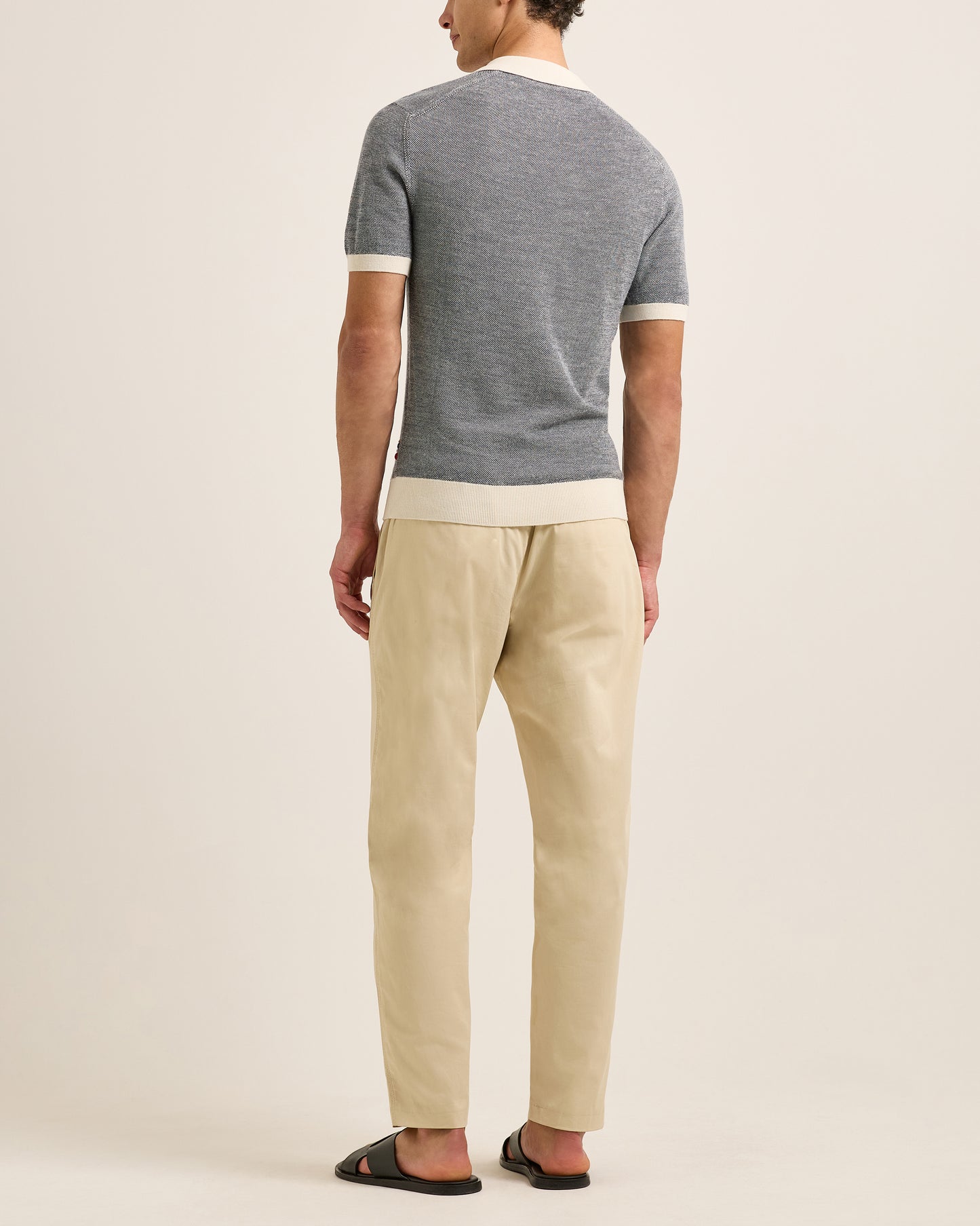 Man wearing a grey polo shirt and beige pants on a plain background