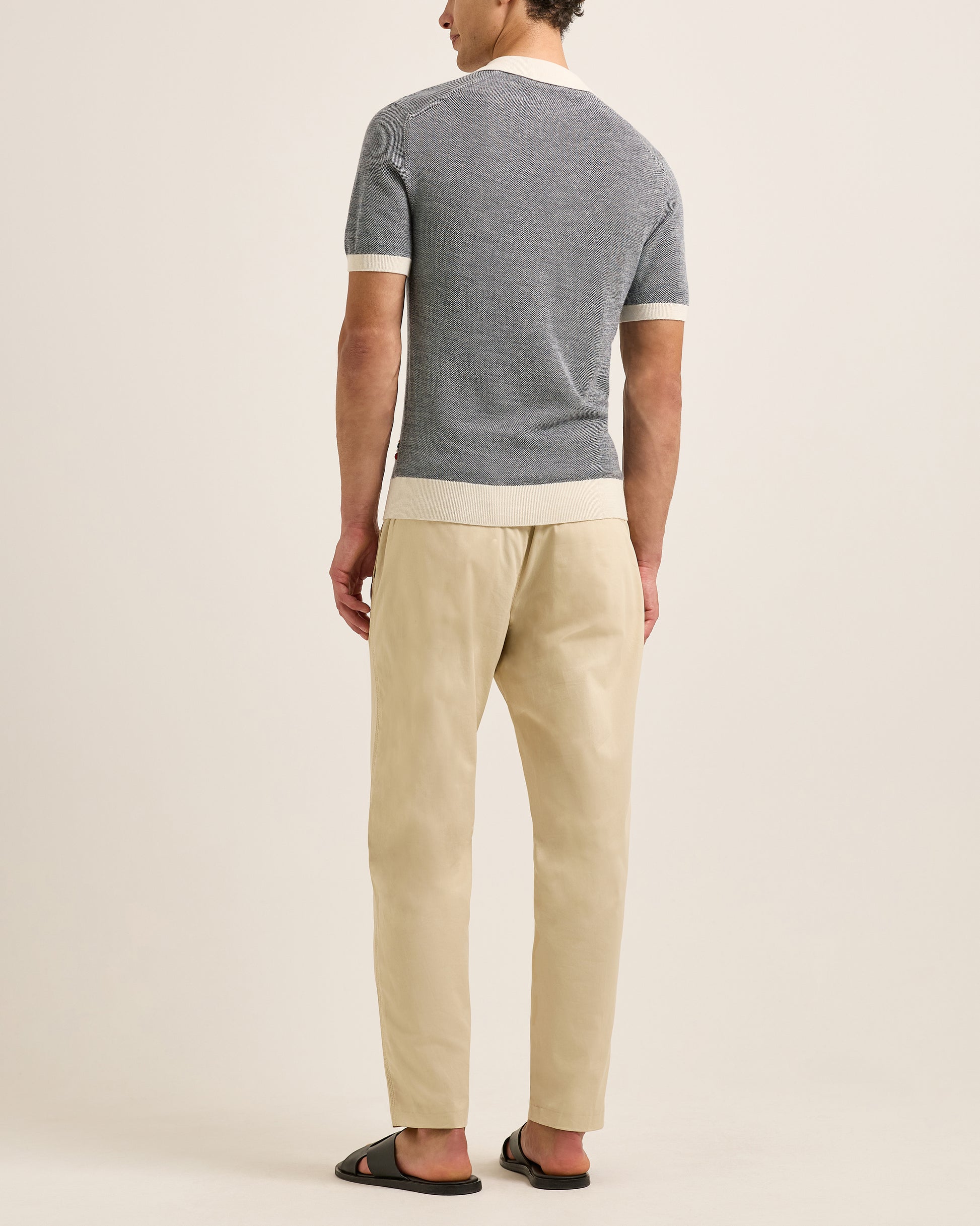 Man wearing a grey polo shirt and beige pants on a plain background