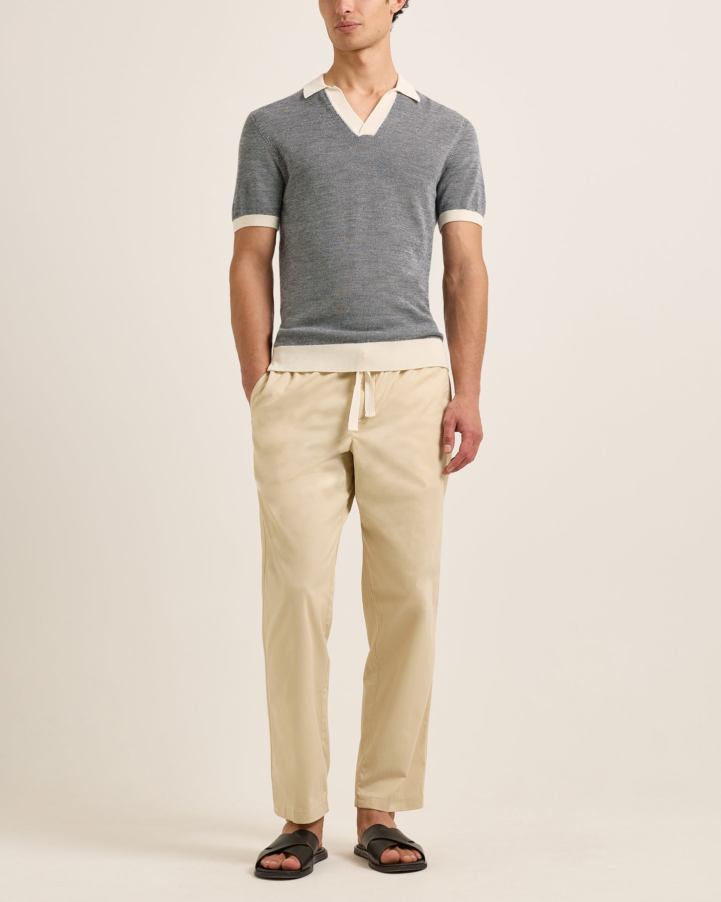 Person wearing a grey polo and beige pants on a plain background