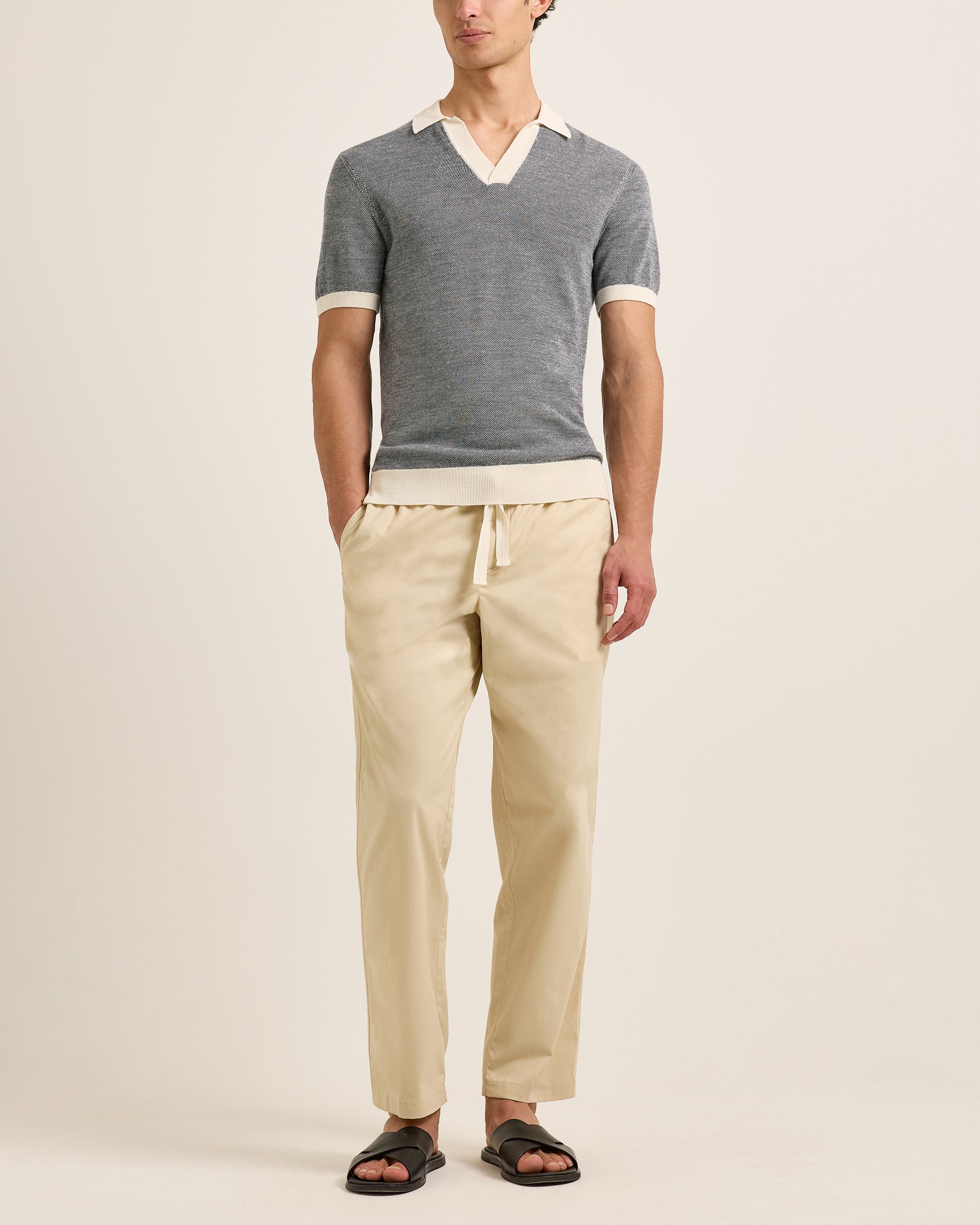 Person wearing a grey polo and beige pants on a plain background