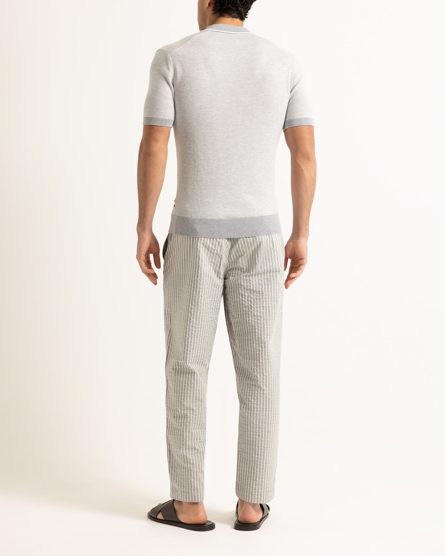 Man wearing a light gray short-sleeve shirt and checkered pants on a white background