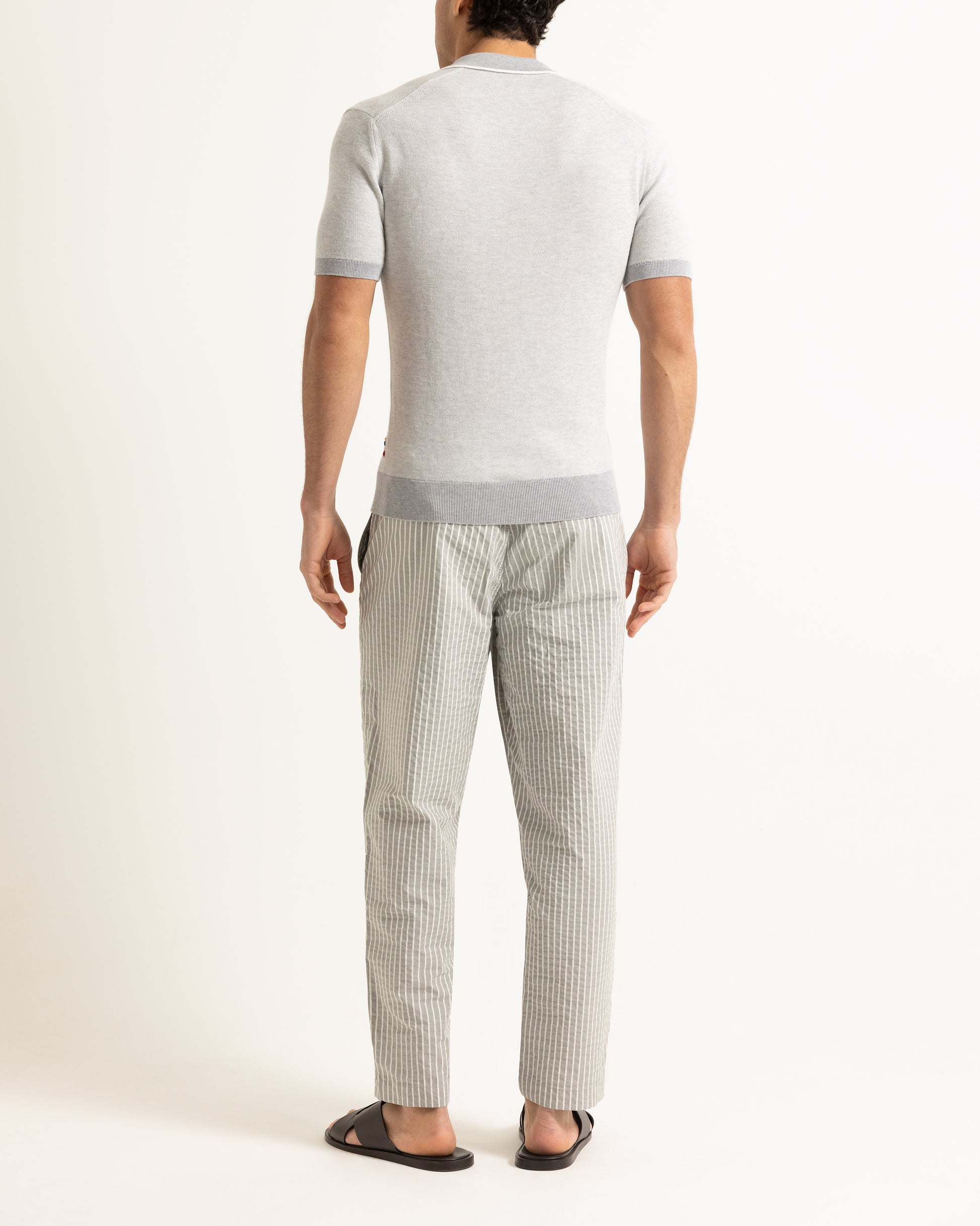 Man wearing a light gray short-sleeve shirt and checkered pants on a white background