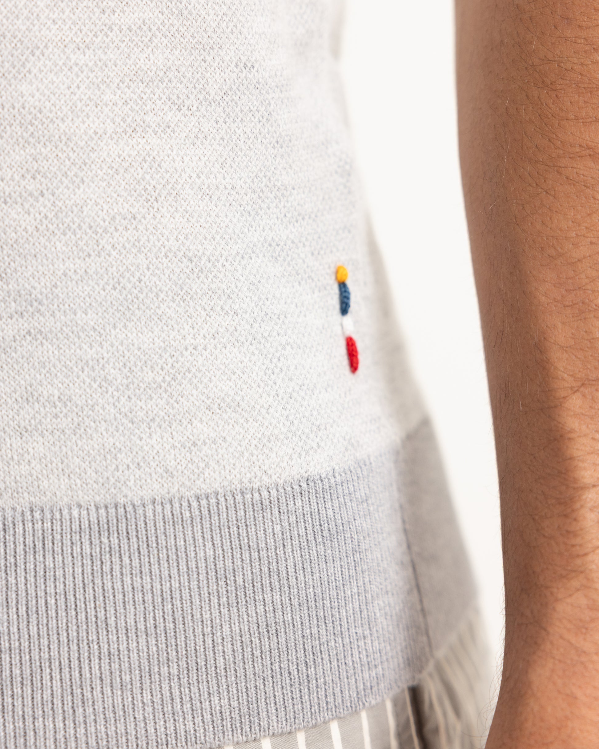 Close-up of a light gray sweater with colorful embroidered design on a person wearing it.