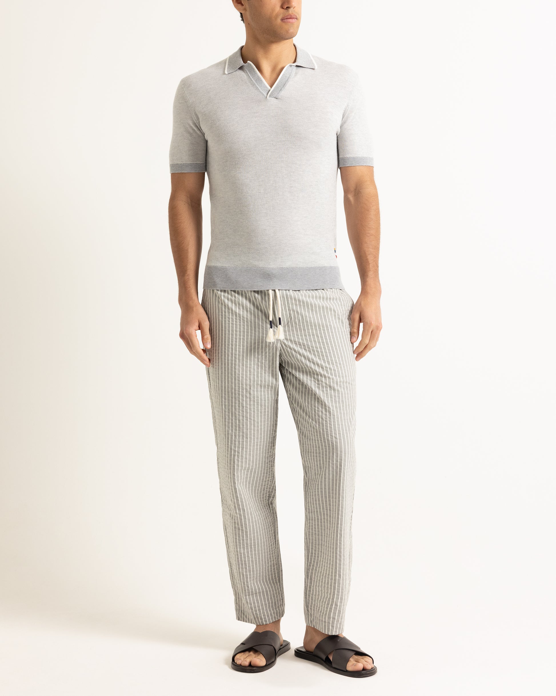 Man wearing light grey polo shirt with grey striped trousers on a plain background