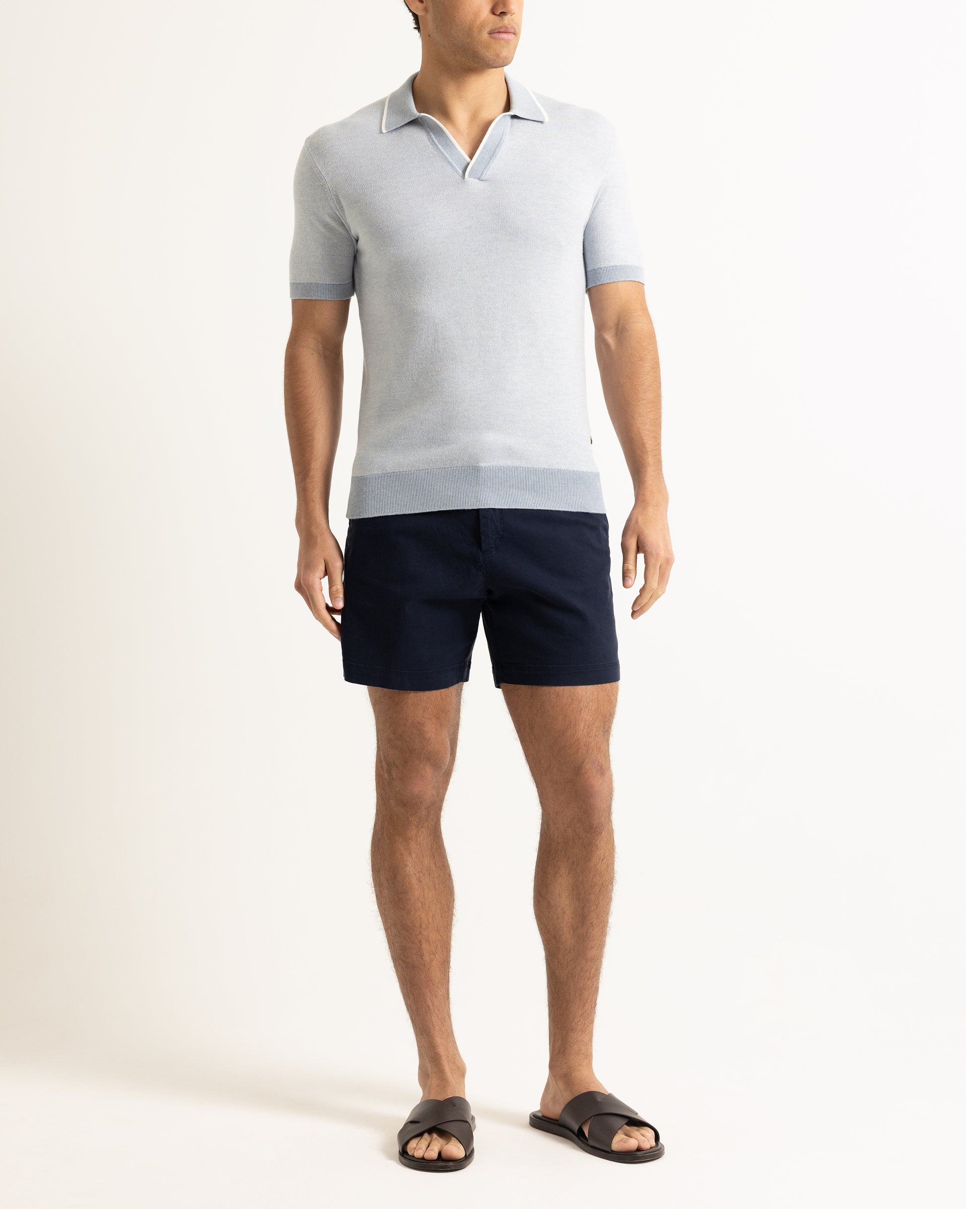 Man wearing a light gray polo shirt and navy shorts on a white background