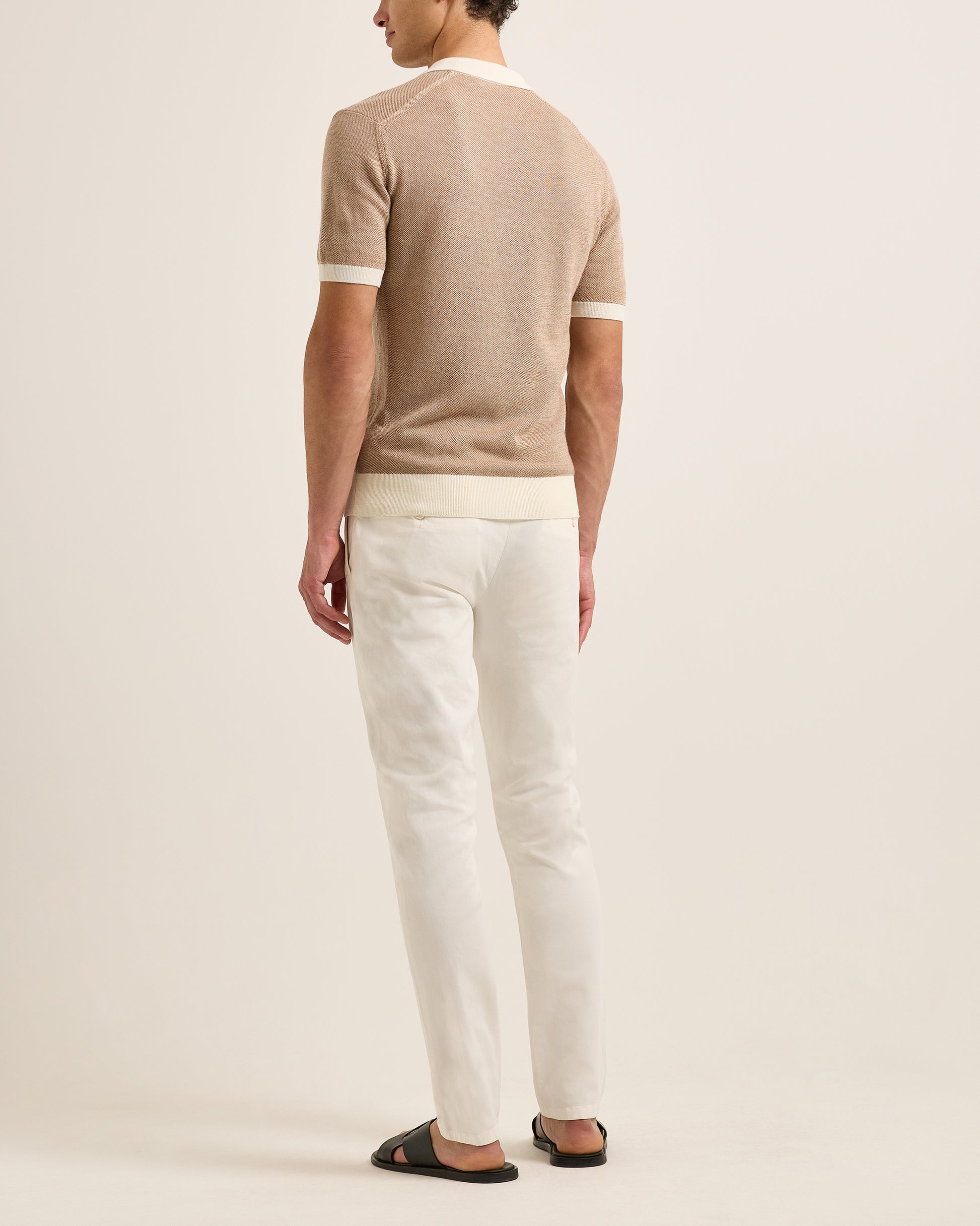 wearing a beige polo and white pants on a plain background