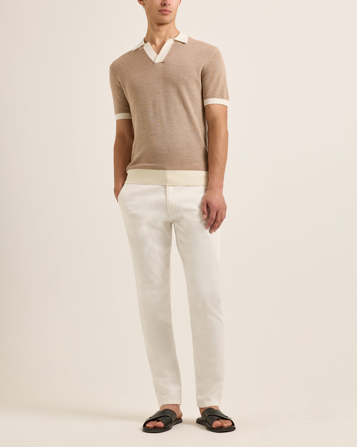 Person wearing a beige short-sleeve polo shirt and white pants on a plain background