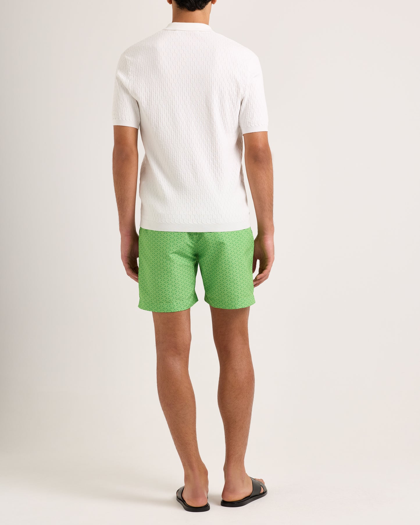 Person wearing a white shirt and green patterned shorts on a plain background