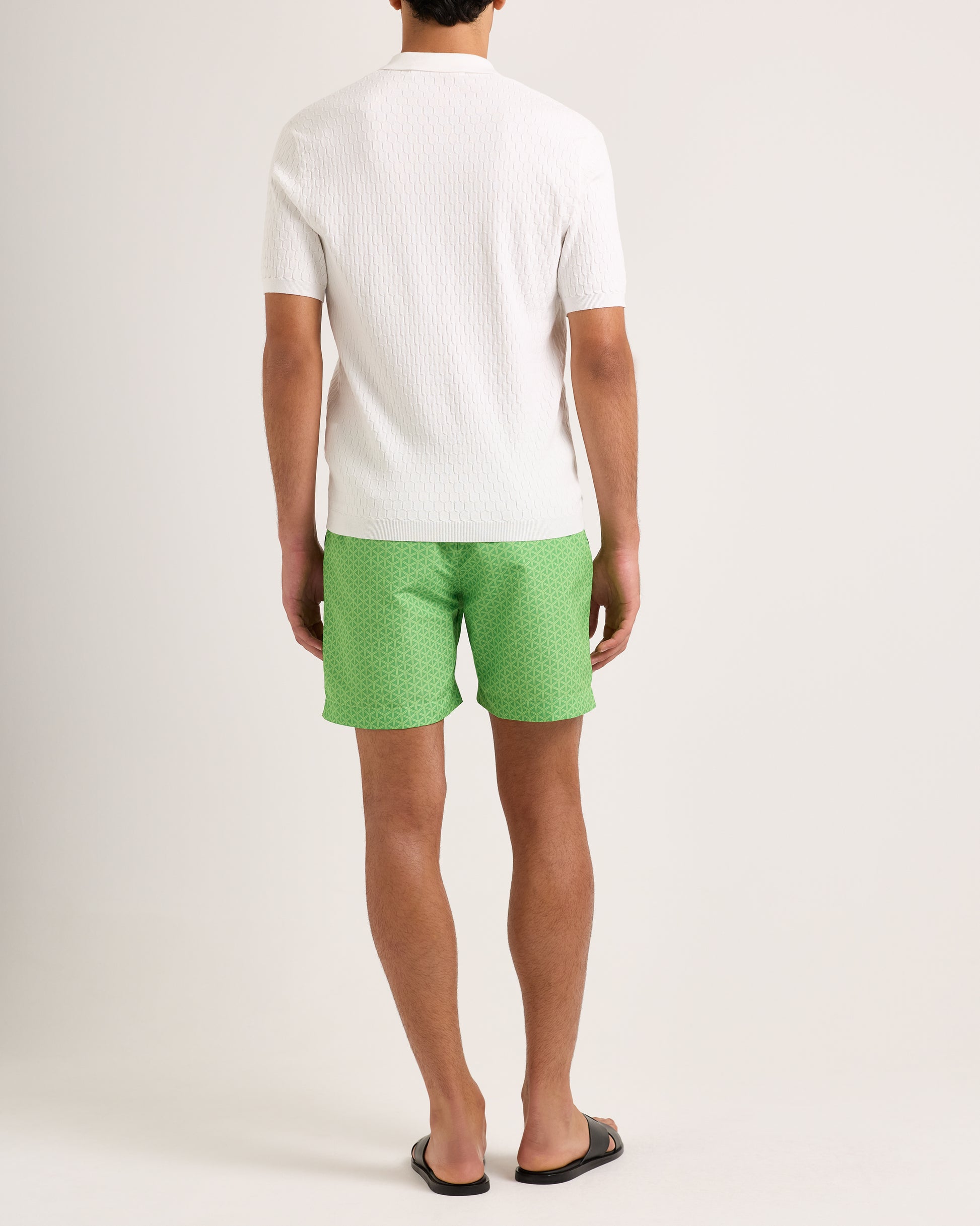 Person wearing a white shirt and green patterned shorts on a plain background