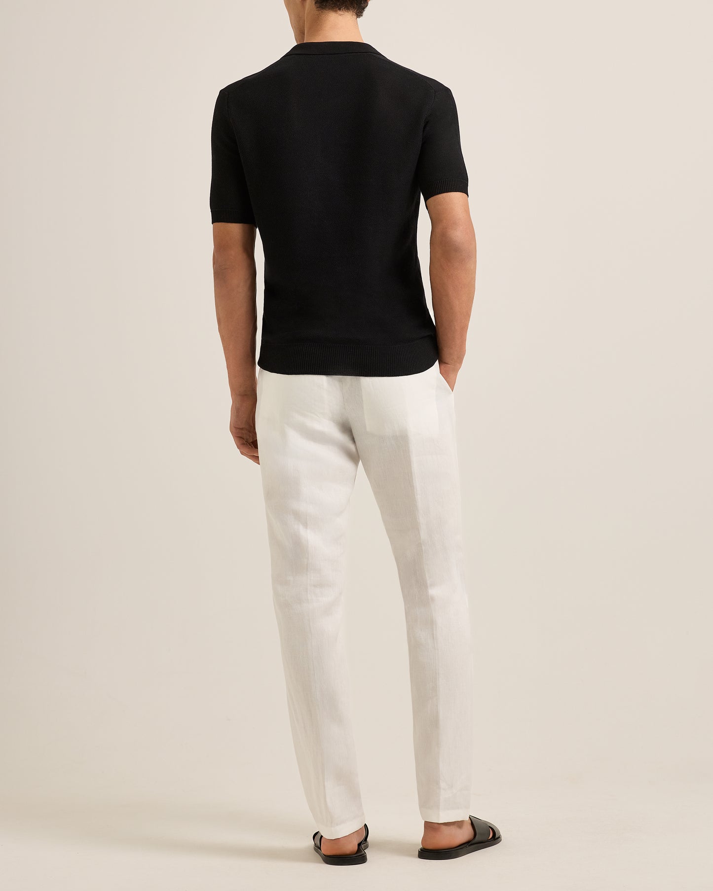 Person wearing a black polo shirt and white pants on a plain background