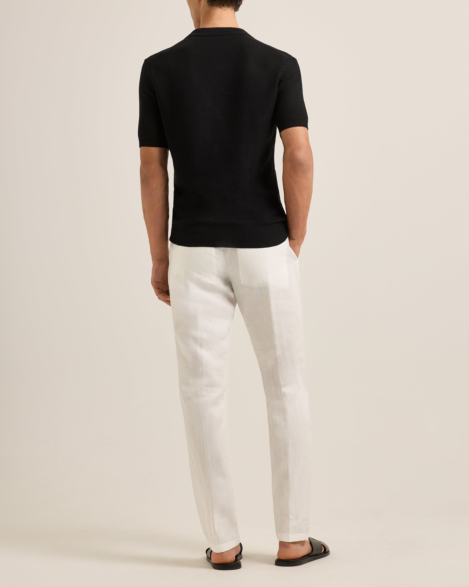 Person wearing a black polo shirt and white pants on a plain background