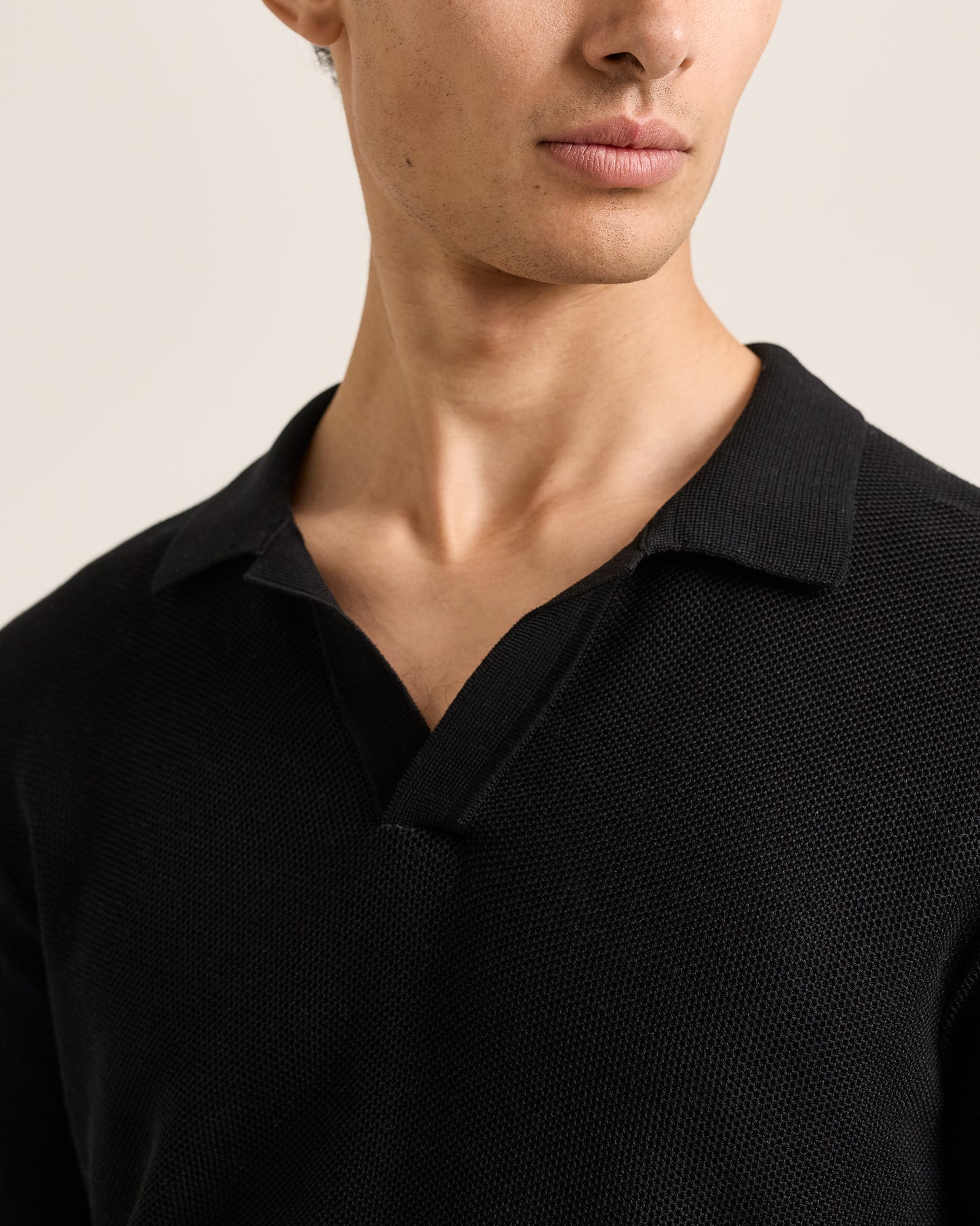 Close-up of a person wearing a black polo shirt against a neutral background