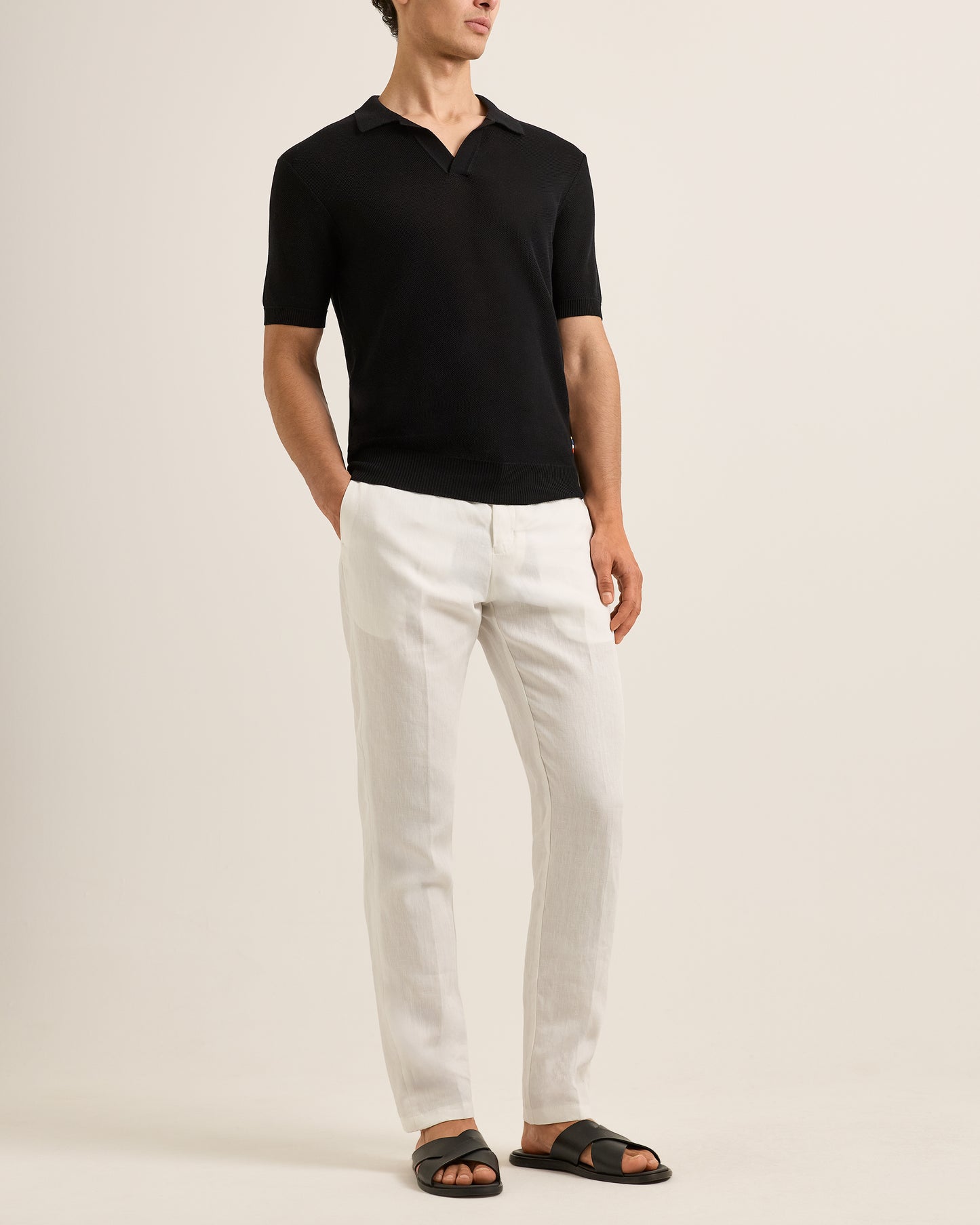 Man wearing a black polo shirt and white pants on a beige background