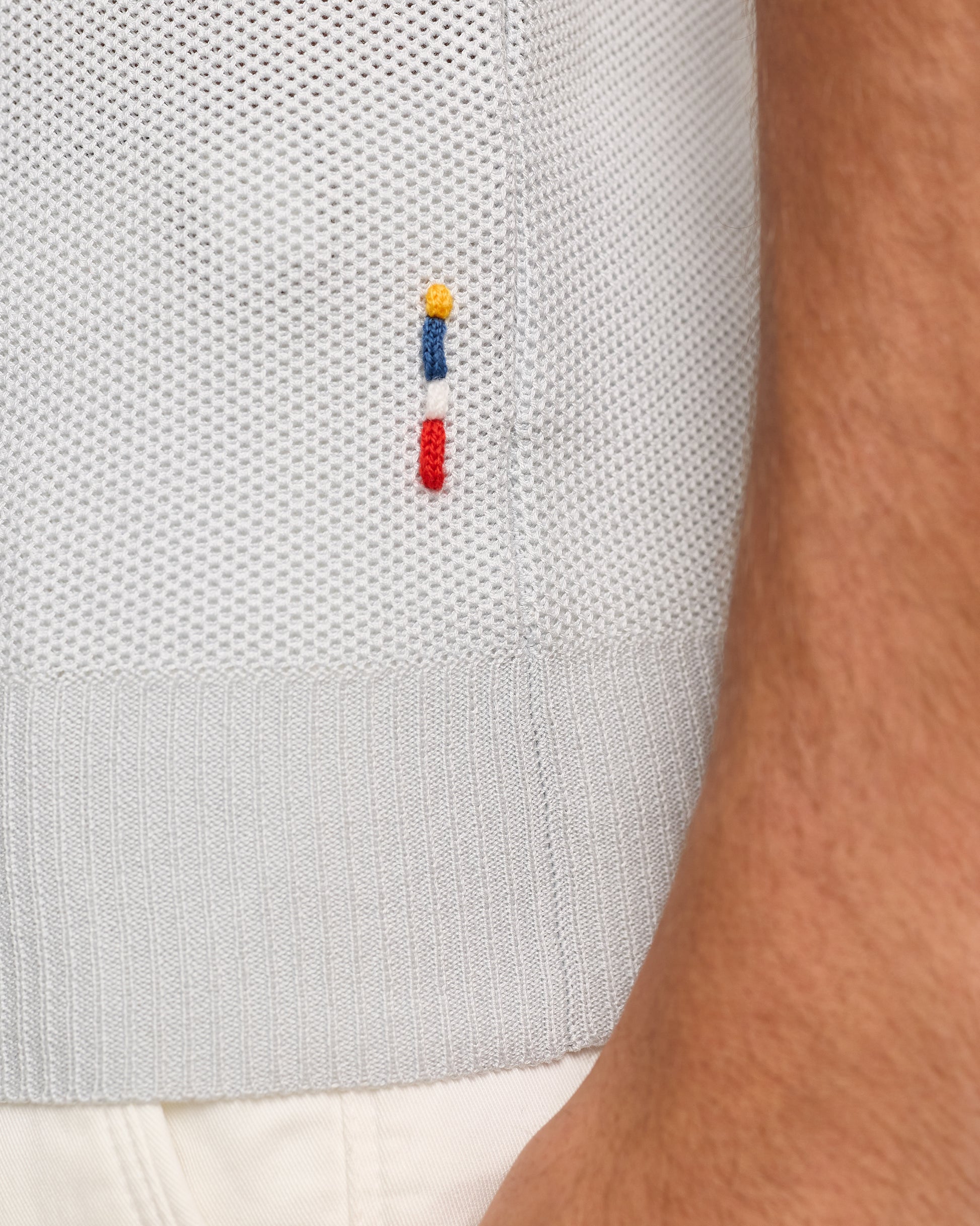 Close-up of  textured polo with a small embroidered logo on a white background.