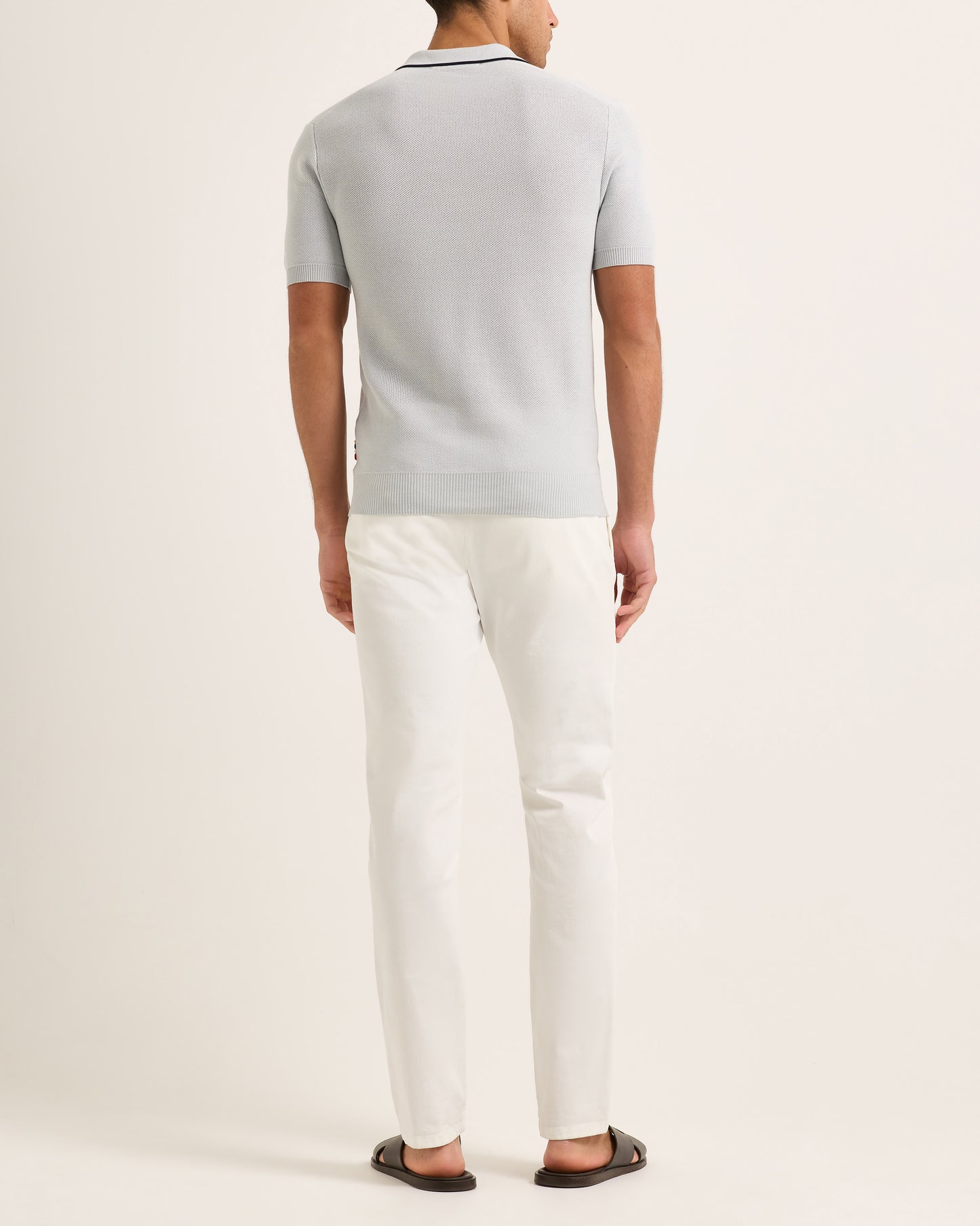 Person wearing a light blue polo shirt and white pants on a plain background