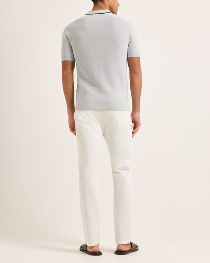 Person wearing a light blue polo shirt and white pants on a plain background