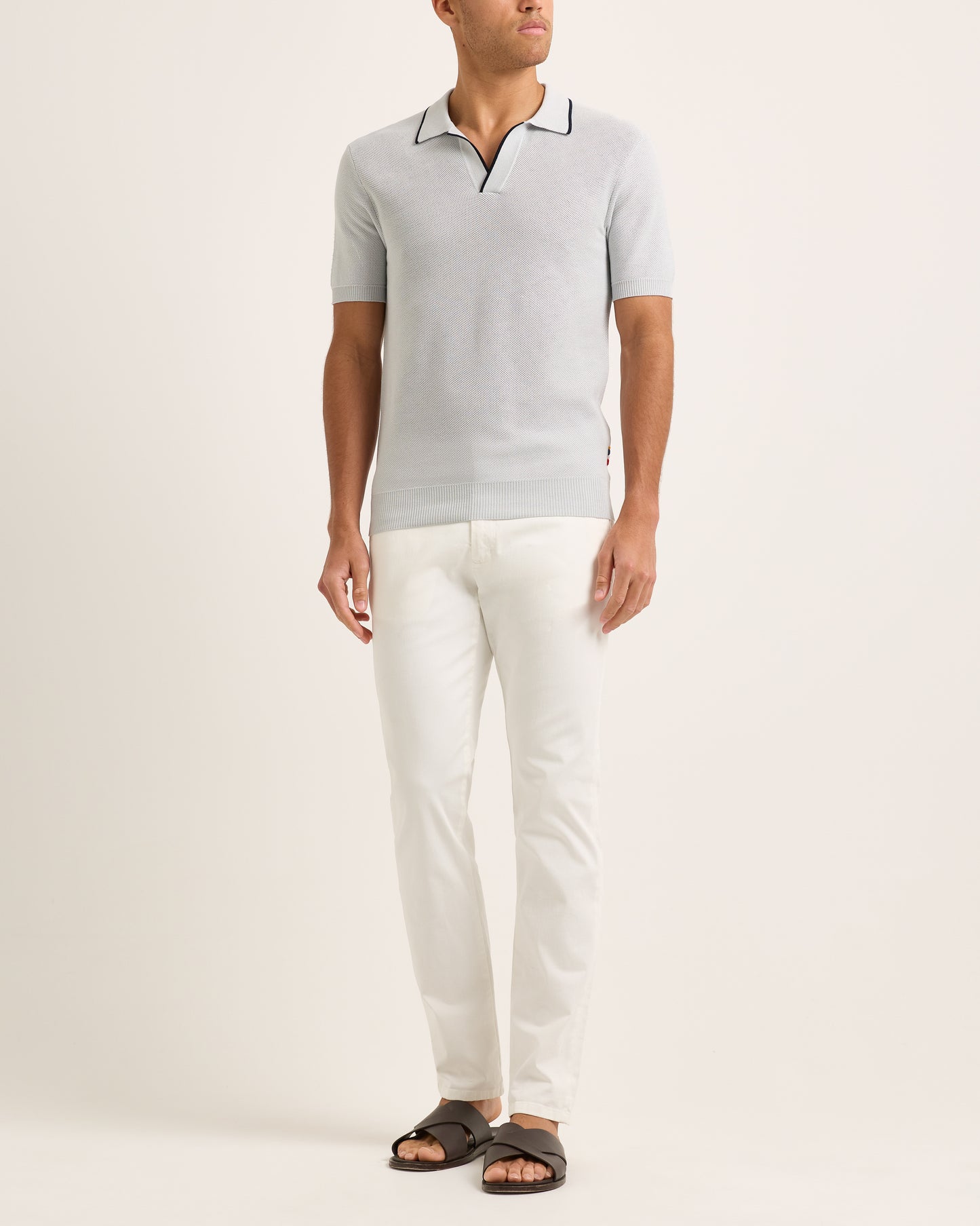 Model wearing a light blue polo shirt and white pants on a plain background
