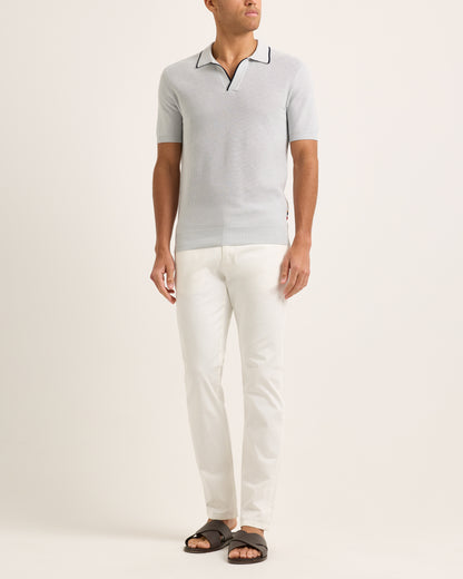 Model wearing a light blue polo shirt and white pants on a plain background