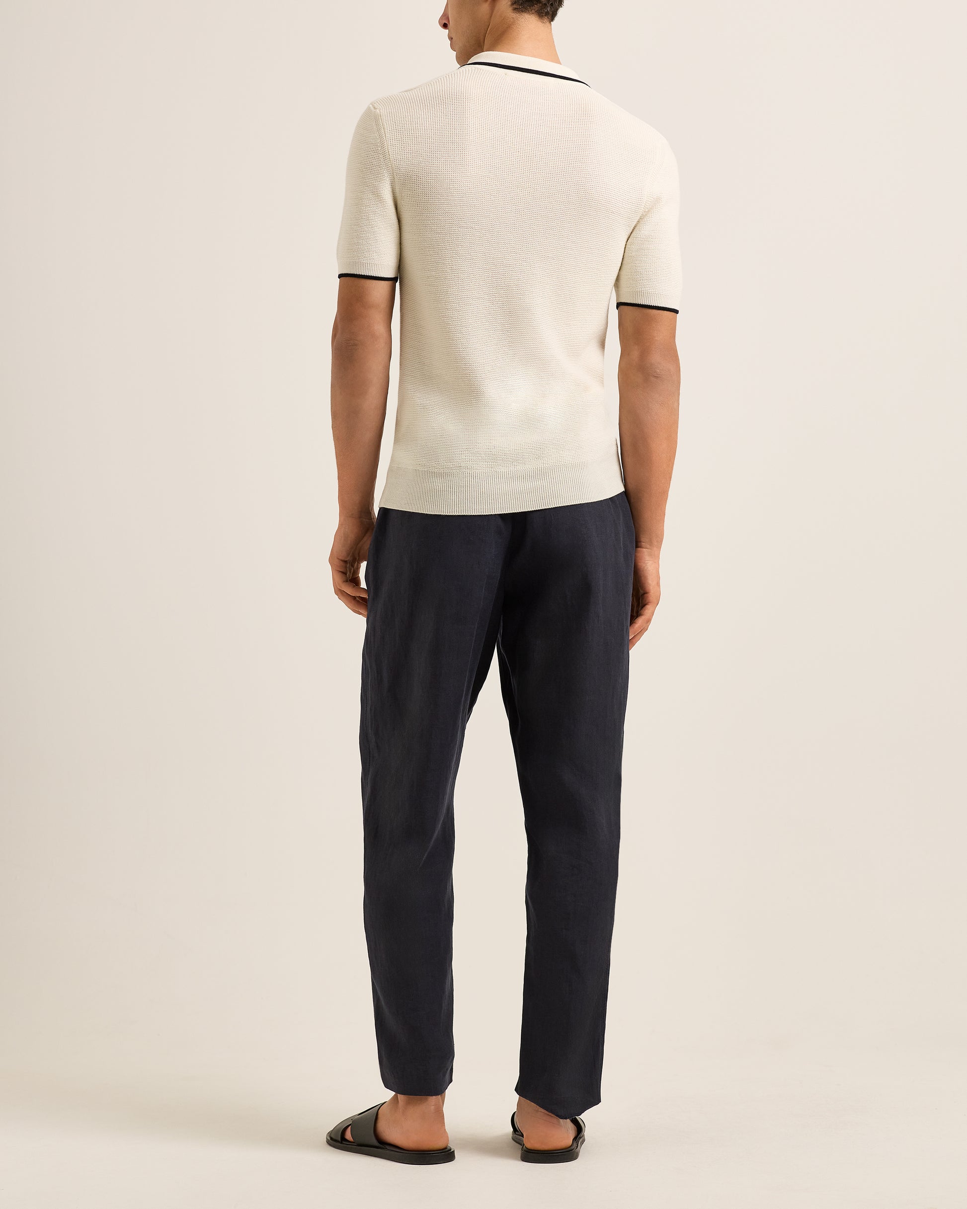 Man wearing a cream sweater and navy pants on a plain background