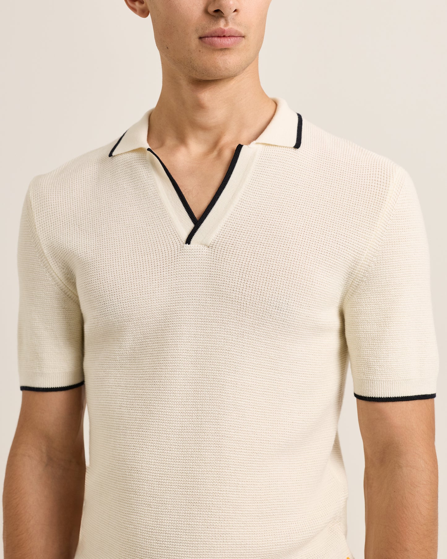 Man wearing a beige short-sleeve knit polo shirt with black trim on a plain background