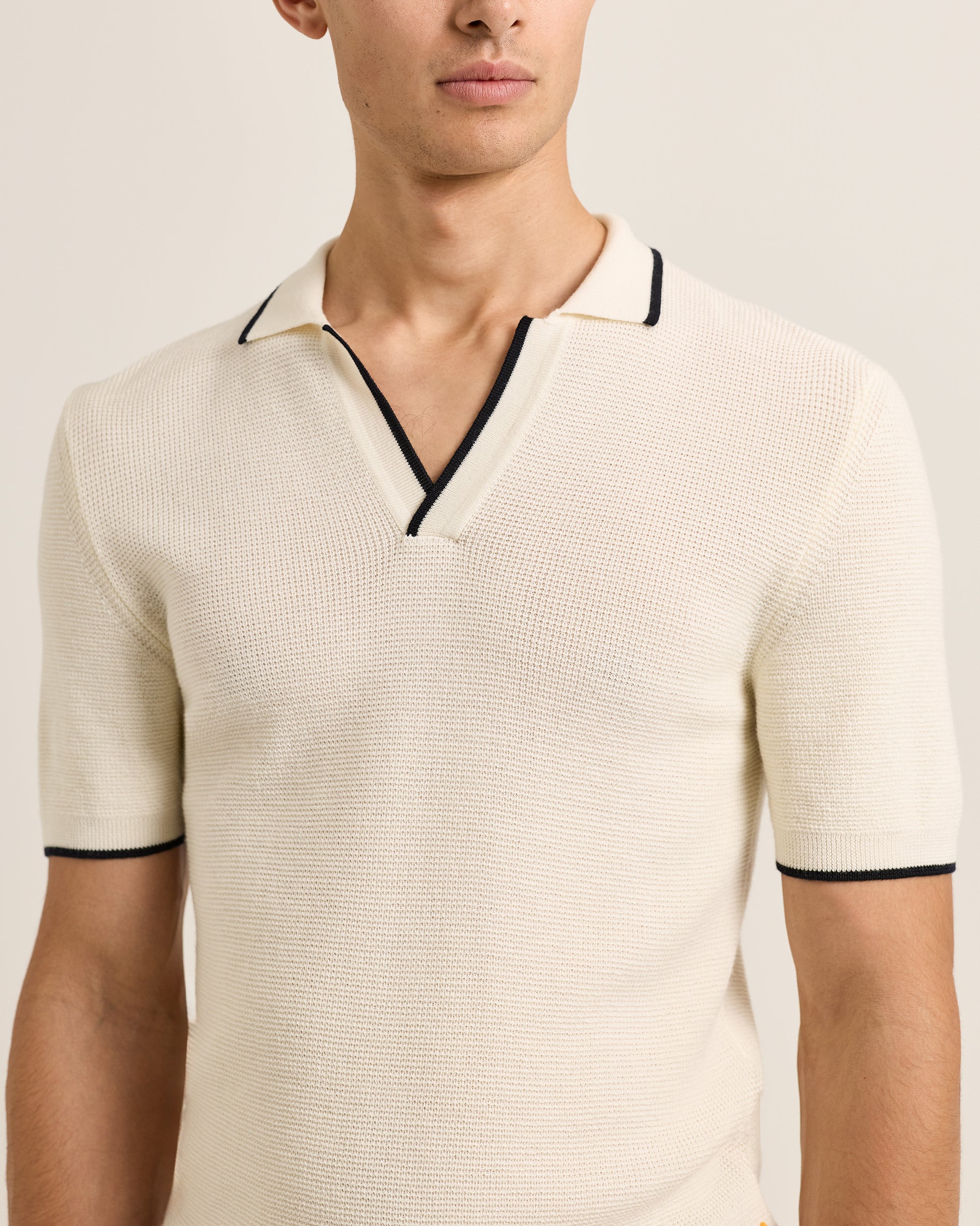 Man wearing a beige short-sleeve knit polo shirt with black trim on a plain background