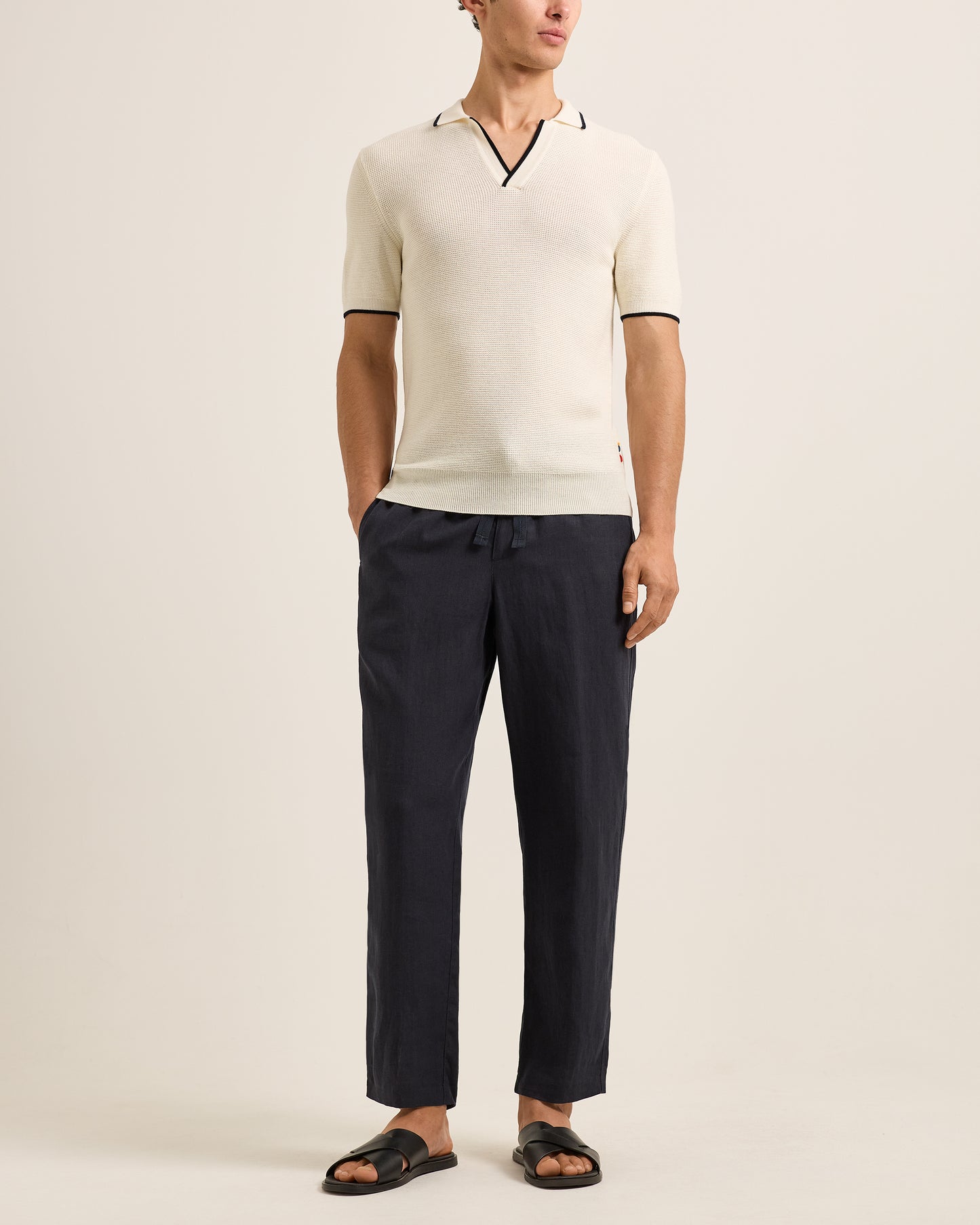 Man wearing a cream sweater and dark pants on a beige background