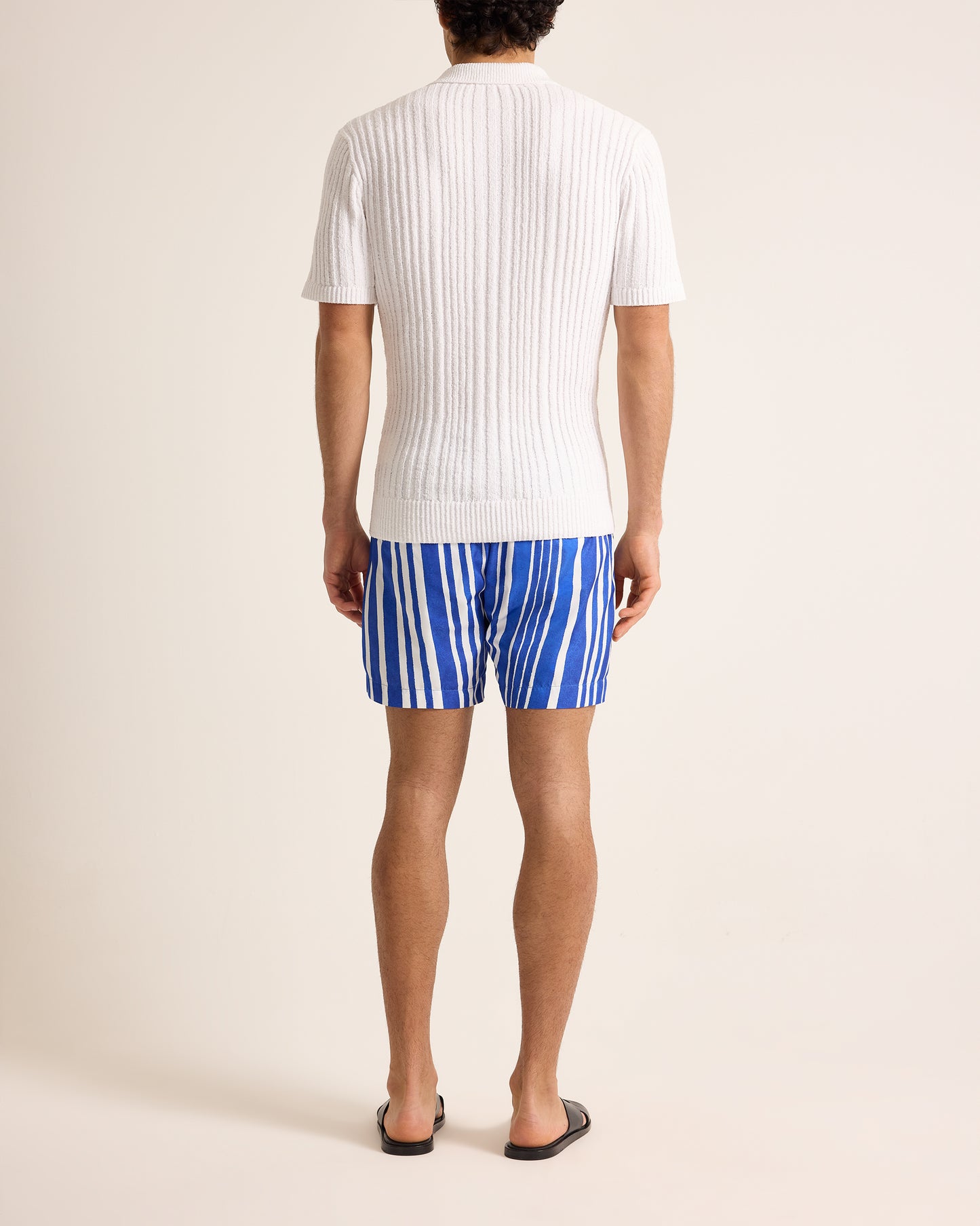 Person wearing a white ribbed t-shirt and blue striped swim shorts on a plain background