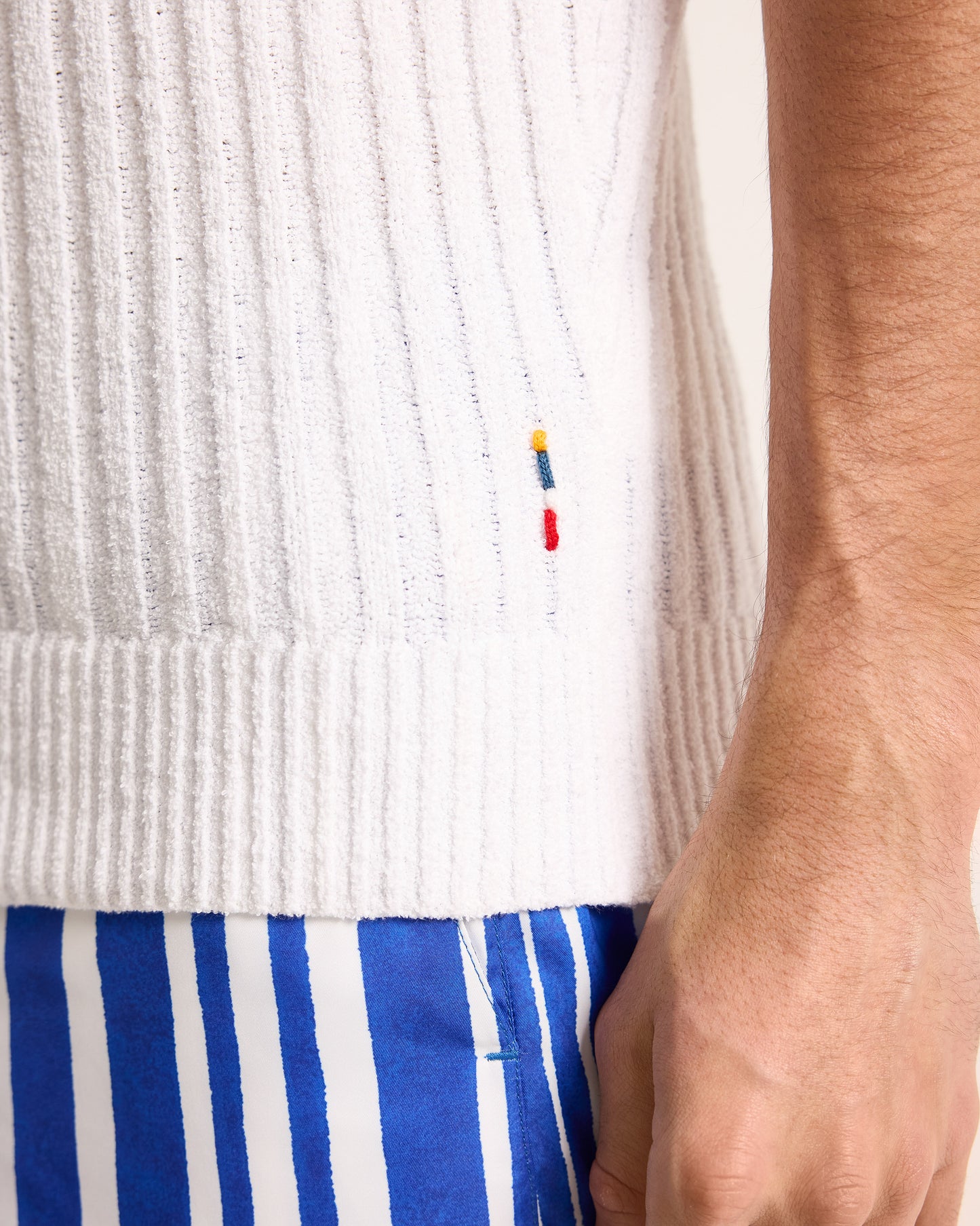 Close-up of a person wearing a white ribbed sweater and blue and white striped shorts.