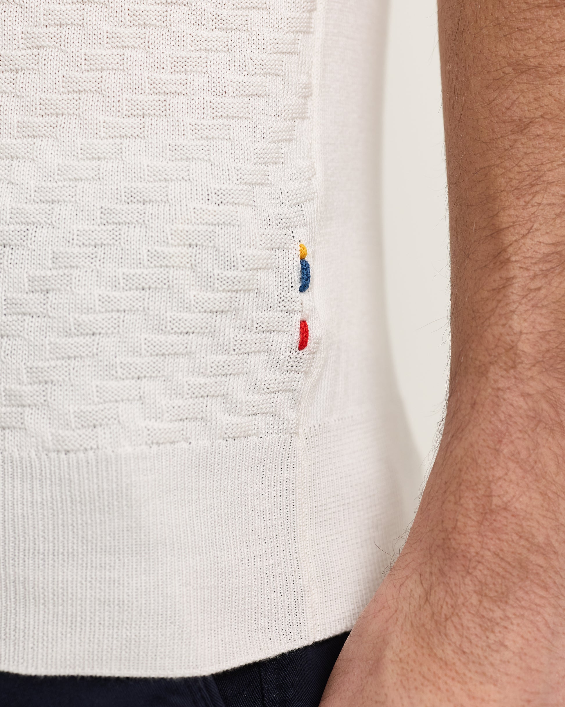 Close-up of a white sweater with embroidered logo on a person wearing it.