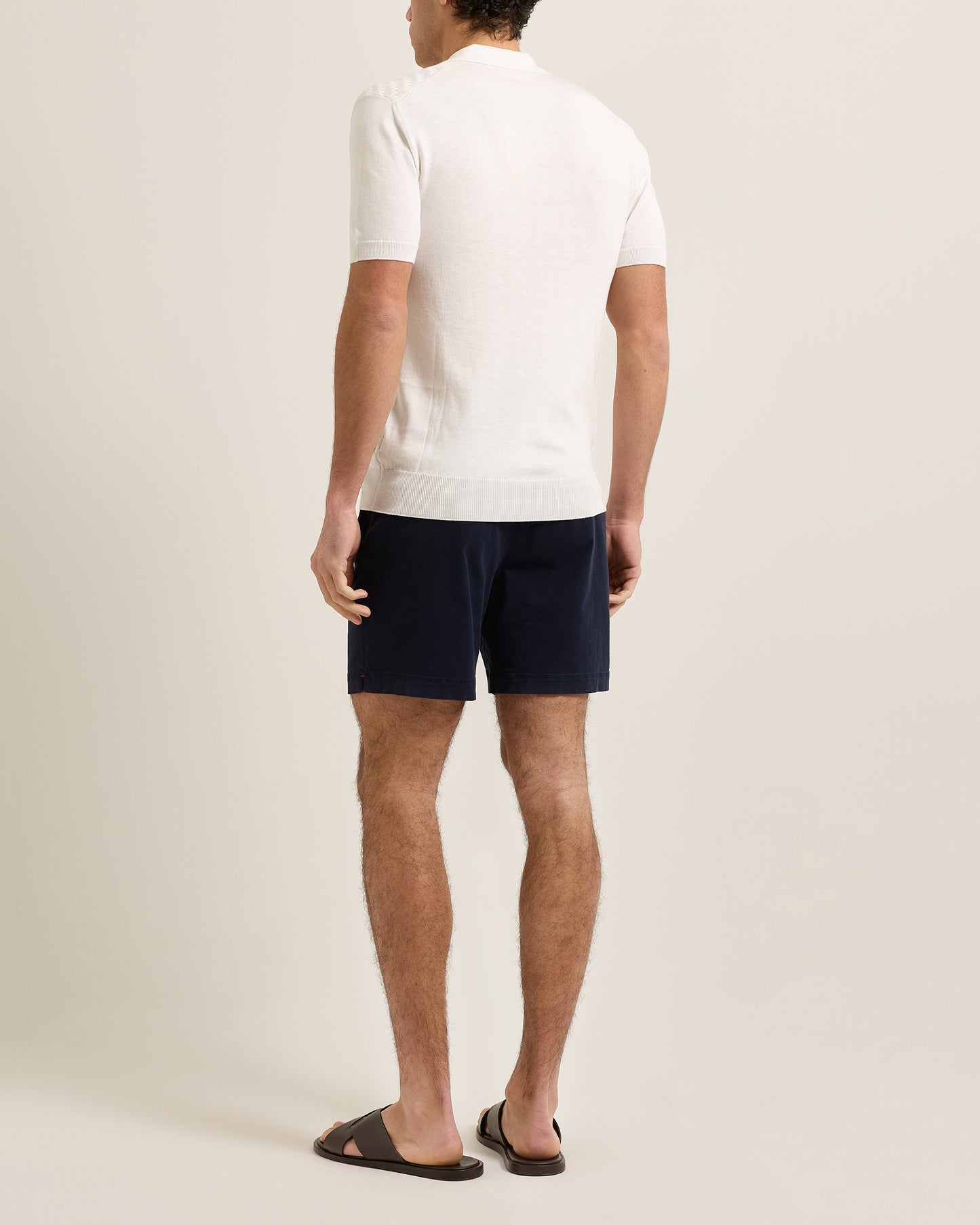 Person wearing navy shorts and a white shirt on a plain background