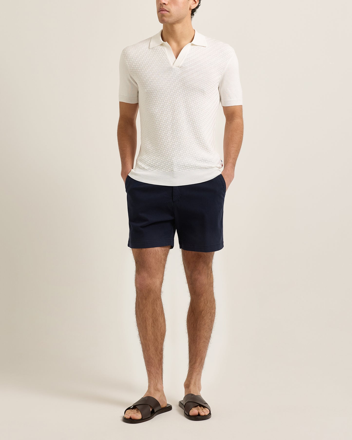 Man wearing a white polo shirt and navy shorts on a plain background