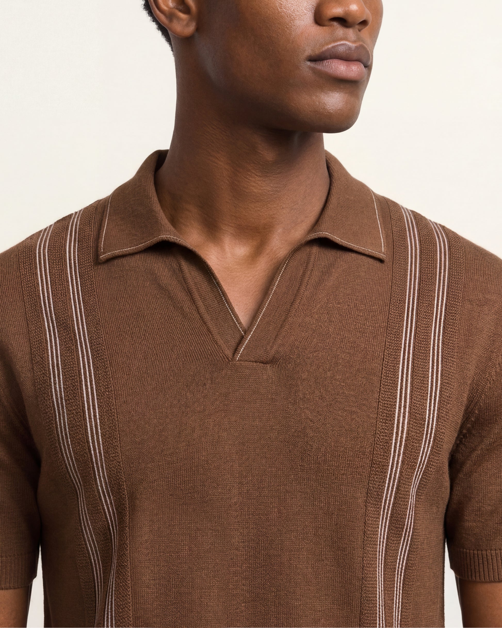 A close-up of a man wearing a brown short-sleeve knit polo shirt with vertical light-colored stripe details on the shoulders and sides, against a plain light background.
