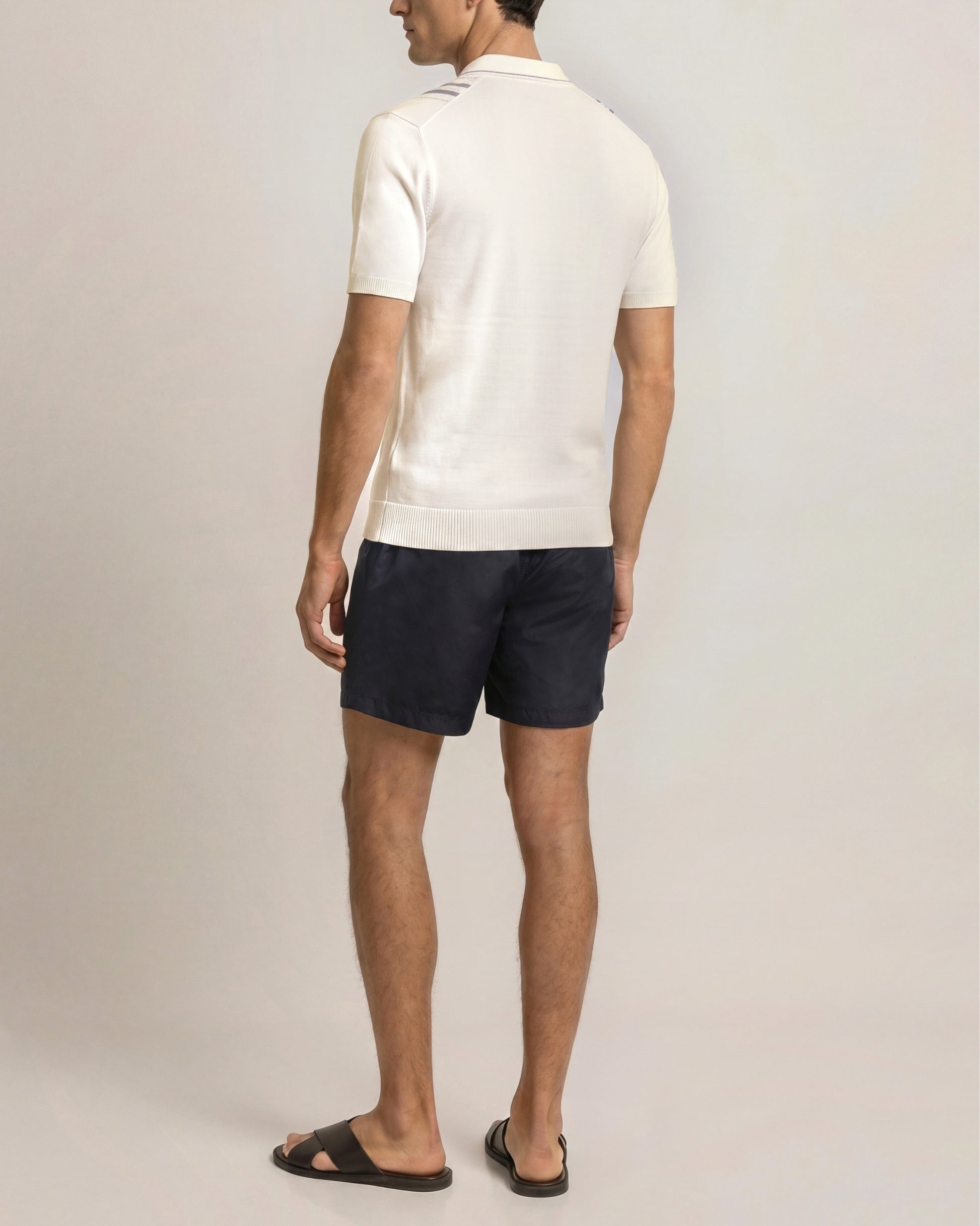 Man wearing a white polo shirt and navy shorts on a plain background