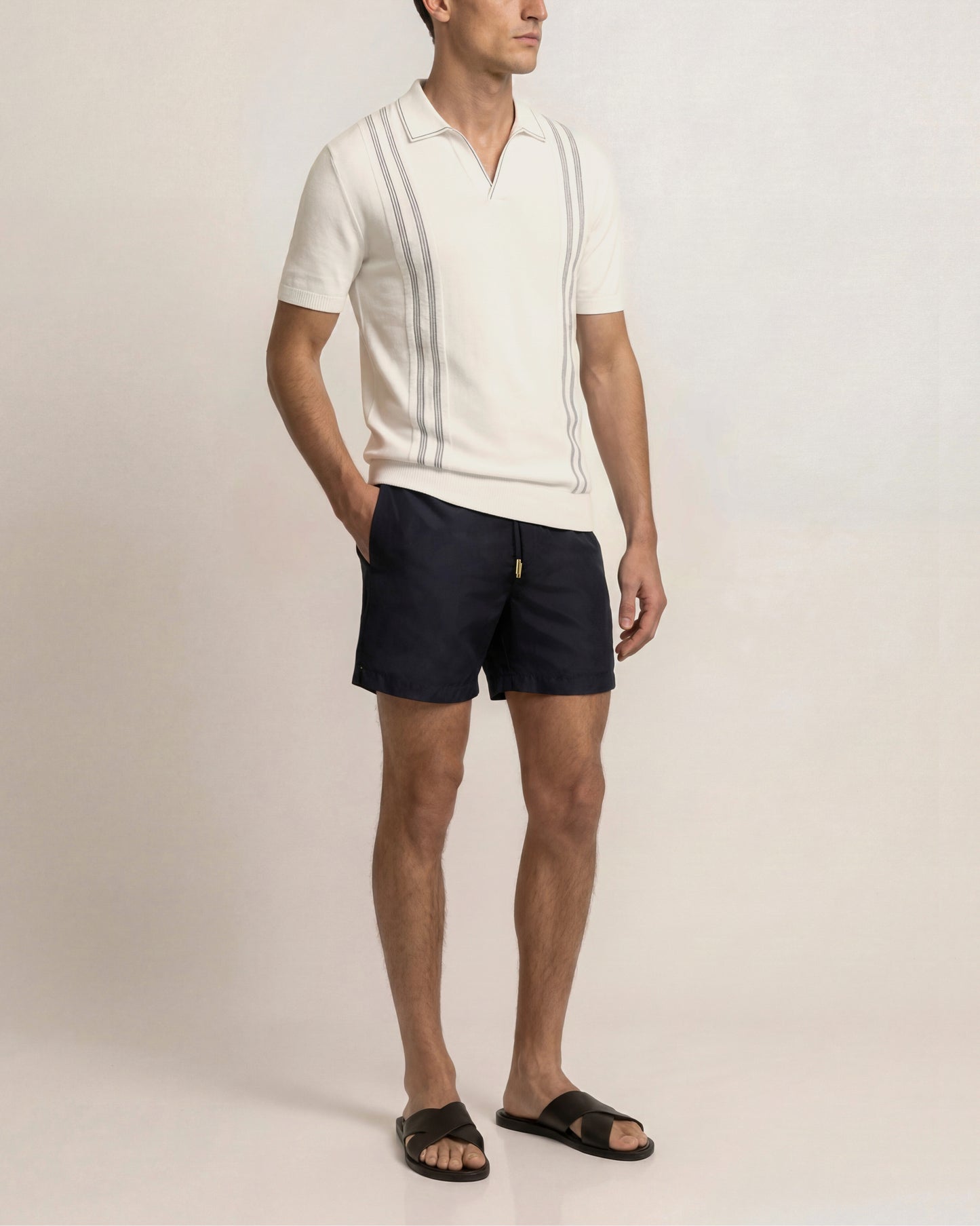 Man wearing a white polo shirt and navy shorts on a plain background