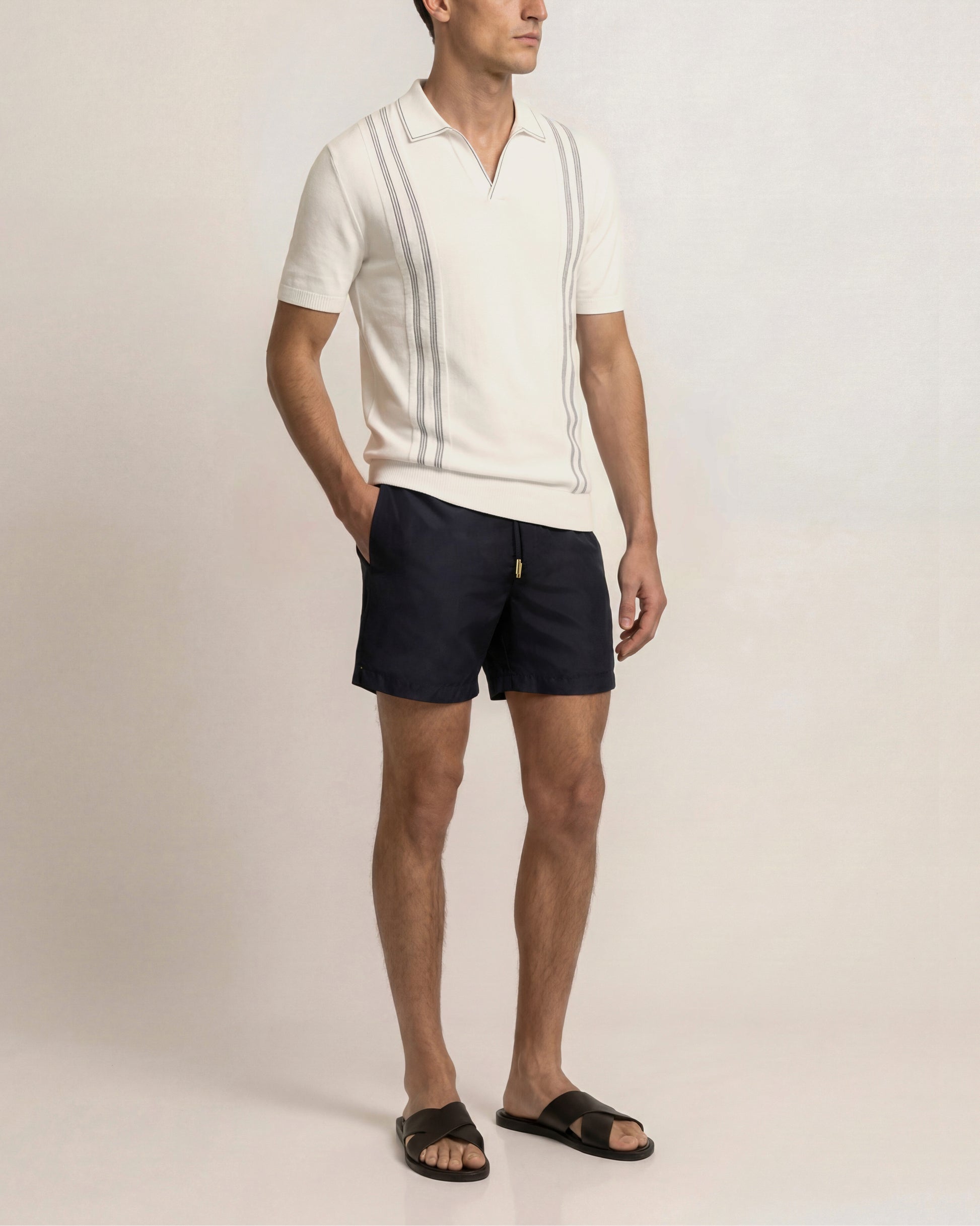 Man wearing a white polo shirt and navy shorts on a plain background