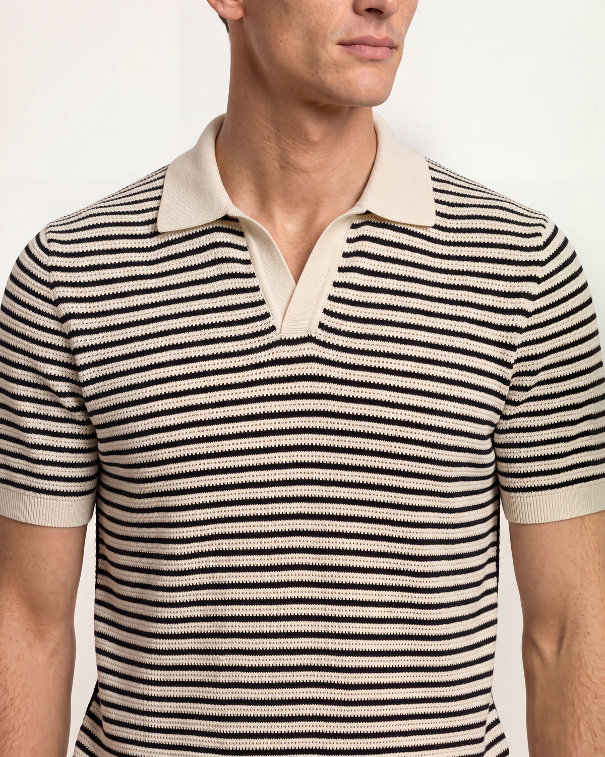 A close-up of a man wearing a short-sleeve knit polo shirt with horizontal black and beige stripes, featuring a solid beige collar and button placket.